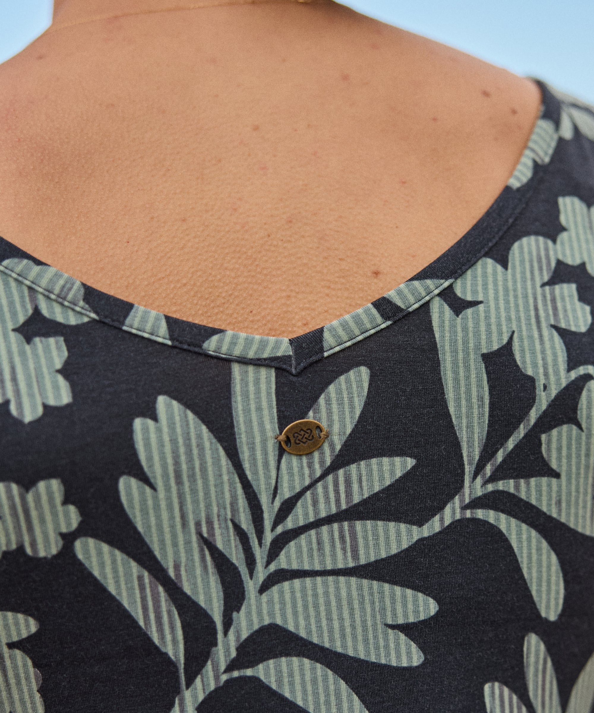 A close up of the back of women's dress. The dress has a floral pattern with a metal endless knot badge stitched on to the back.