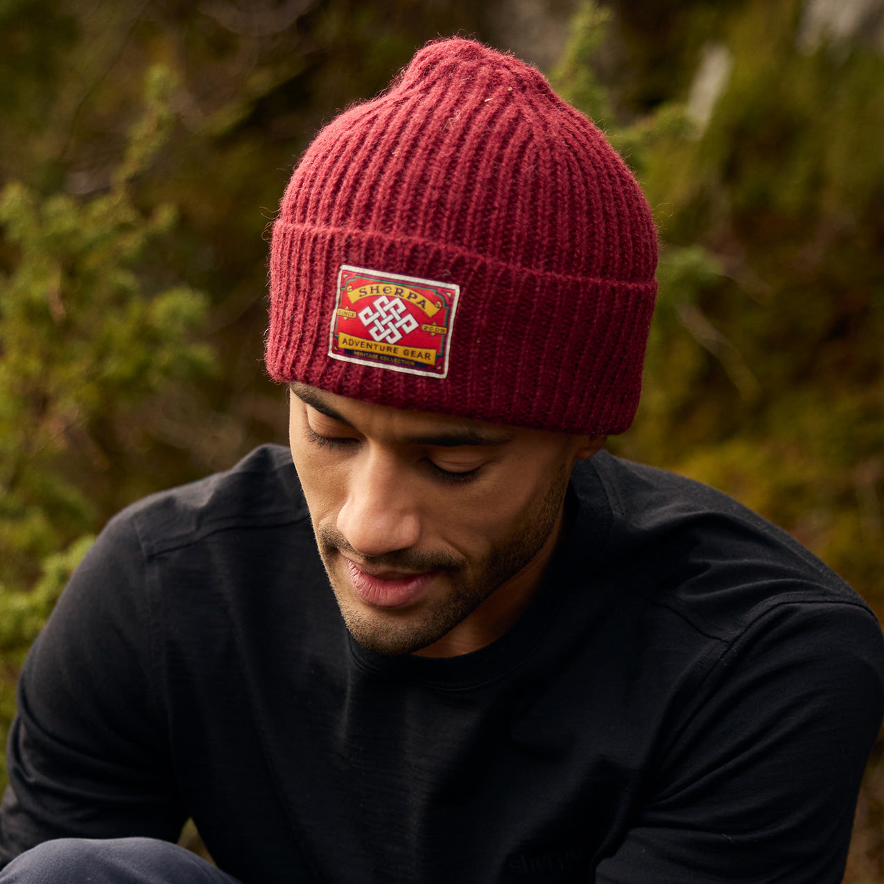 Man in a maroon ribbed knit beanie with an embroidered patch outdoors.