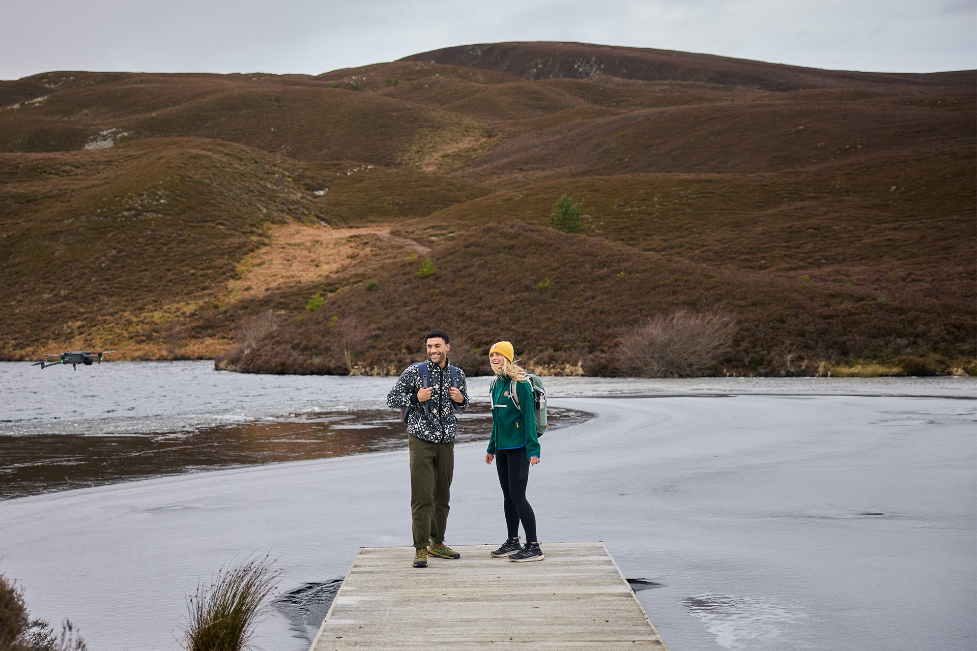 Hikers by a frozen loch in fleece jackets, drone capturing the adventure