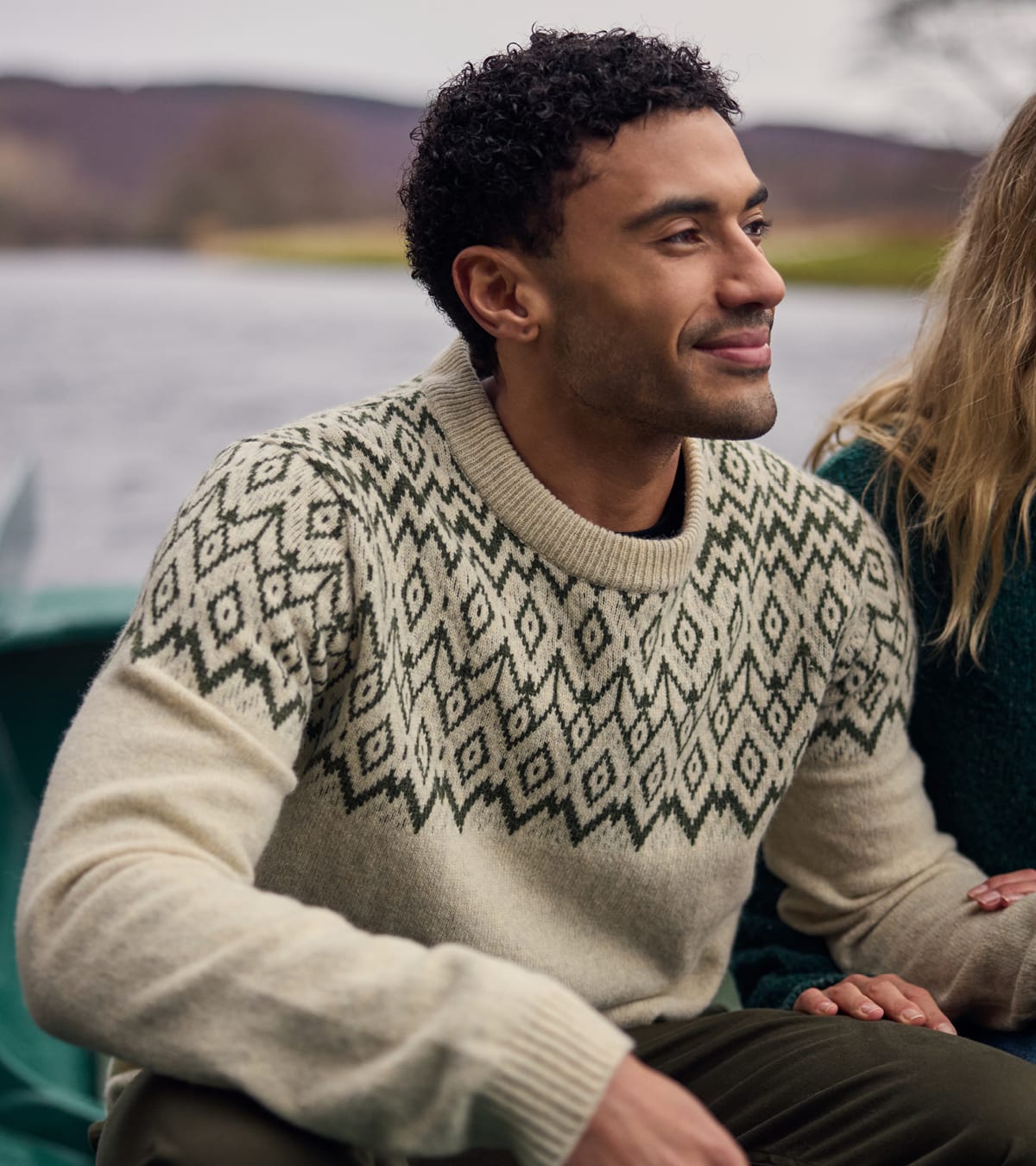 A man wearing a off-white patterned crewneck knit sweater sitting outdoors on a boat.