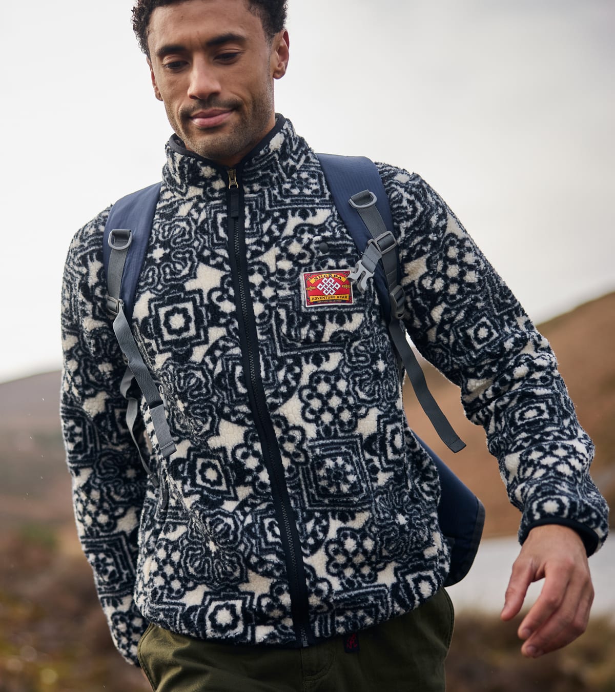 A man wearing a full-zip printed fleece jacket with a backpack outdoors.