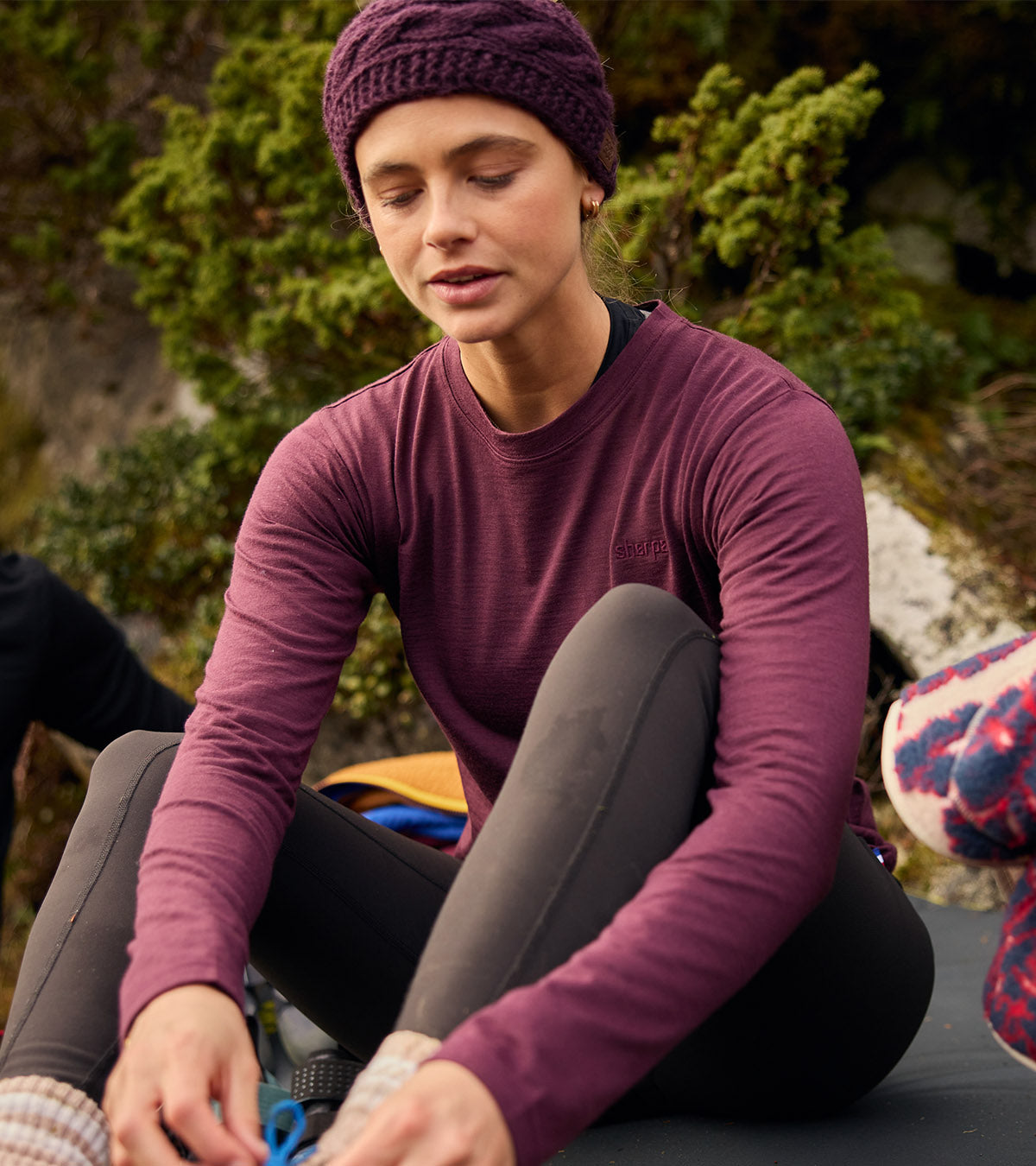 Woman tying boot laces in plum merino top and cable-knit beanie