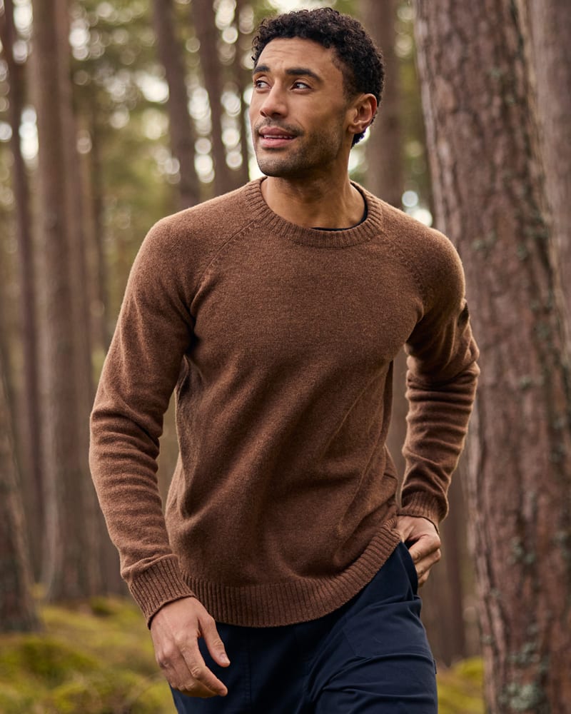 Man walking through pine forest in a heathered brown knit jumper