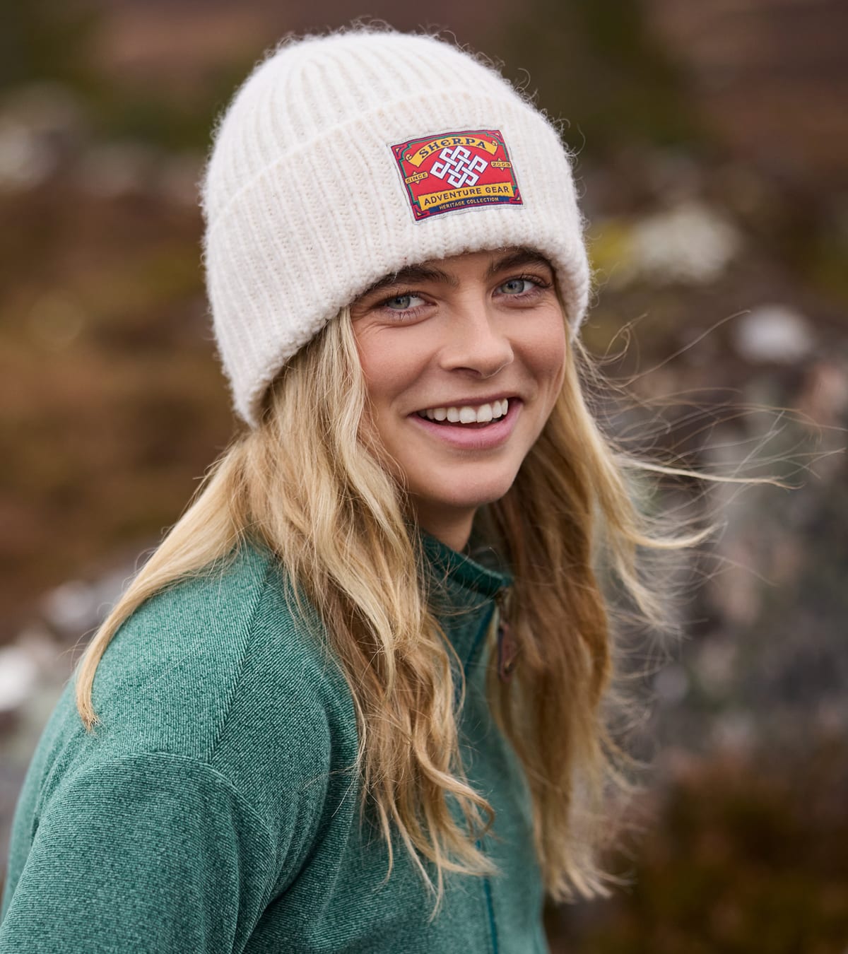 A smiling blonde woman wearing a cream-colored knit beanie.