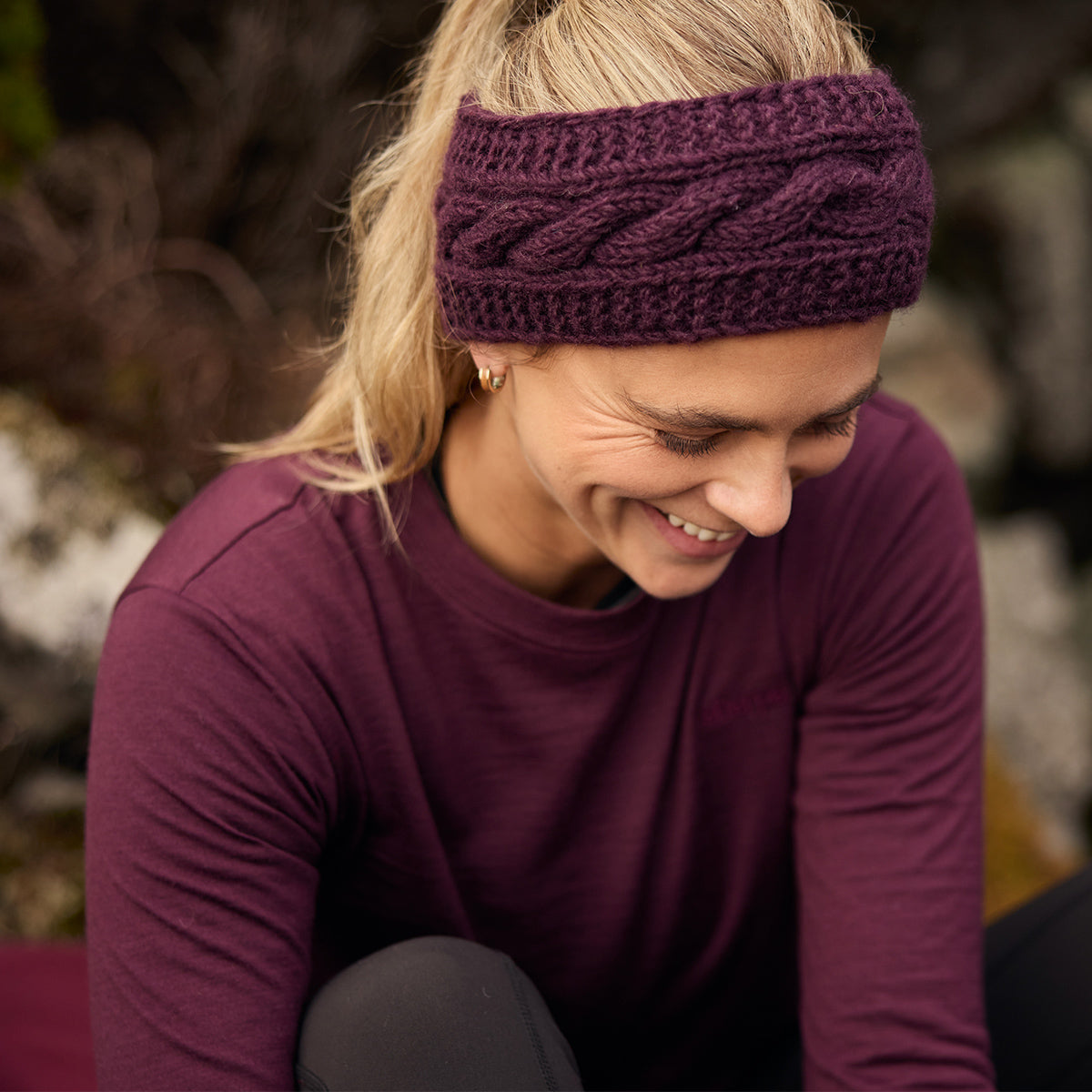 Woman wearing a chunky plum cable-knit headband and matching top outdoors.