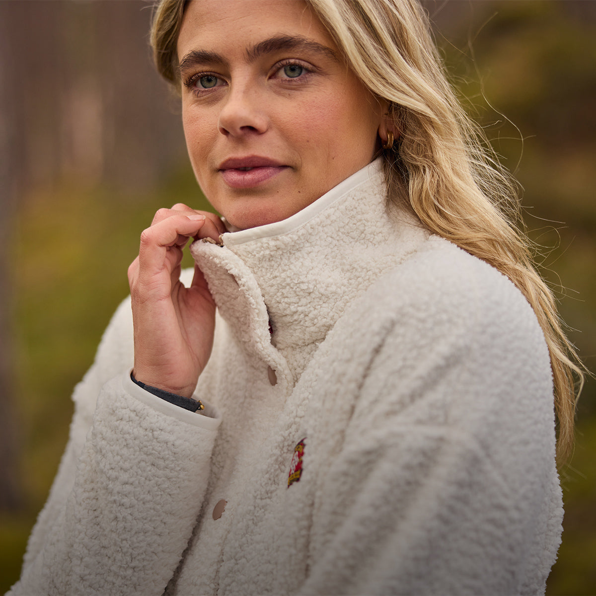 Woman wearing a cream sherpa fleece jacket with a high collar outdoors.