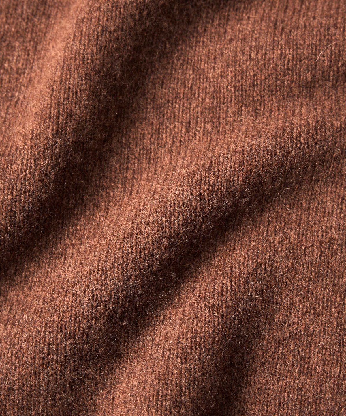 A close-up of a soft, textured knit fabric in a warm rust brown color.