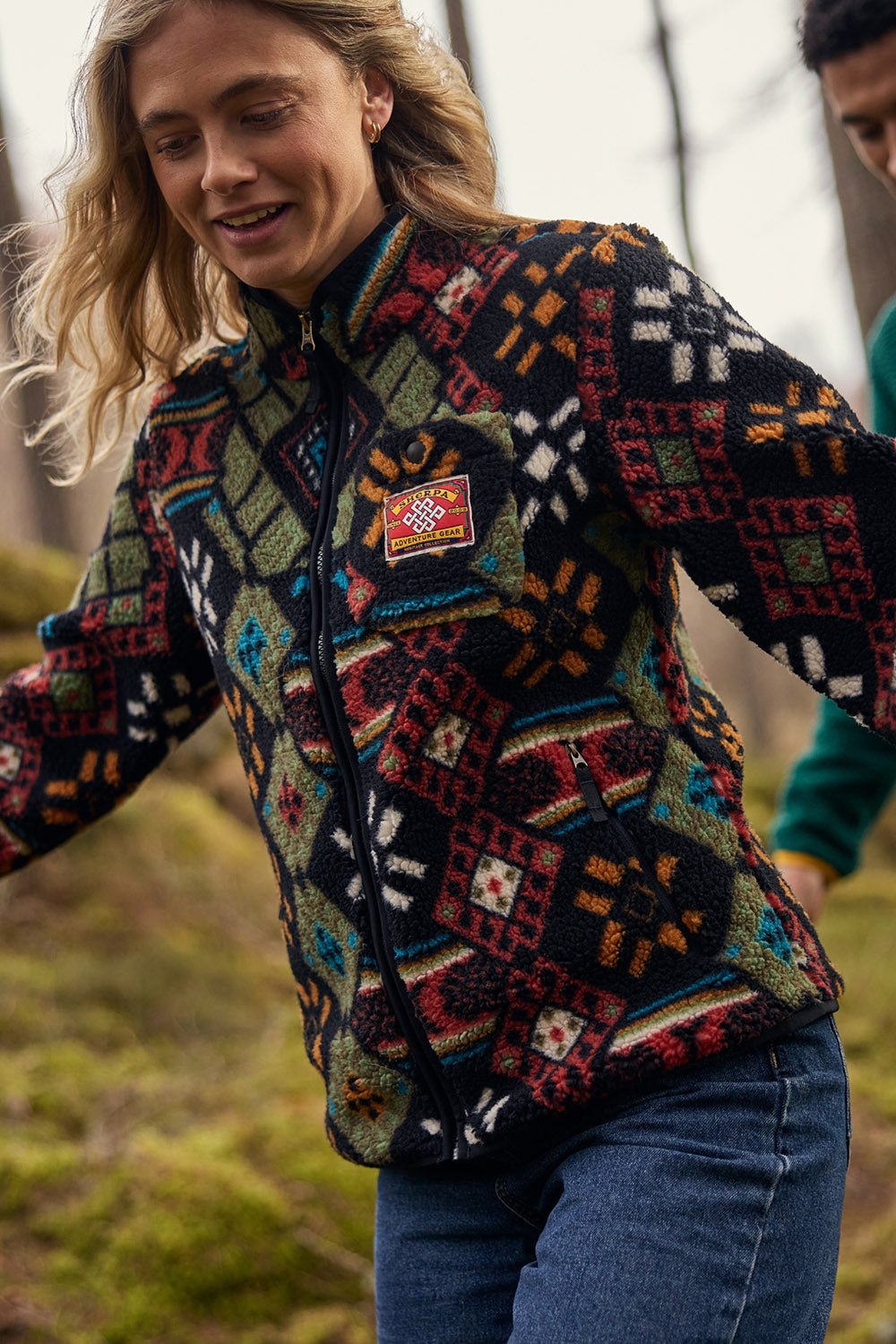 Woman wearing a colorful geometric patterned fleece jacket with logo patch.