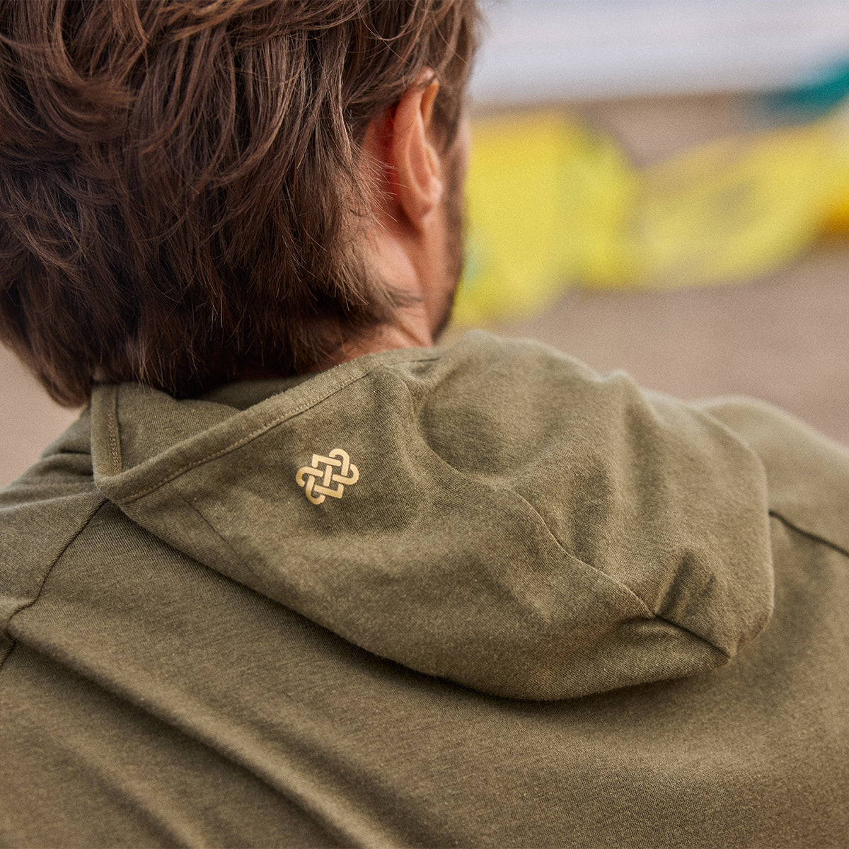 A close of a person wearing a green hoodie with a gold endless knot logo, facing away from the camera.