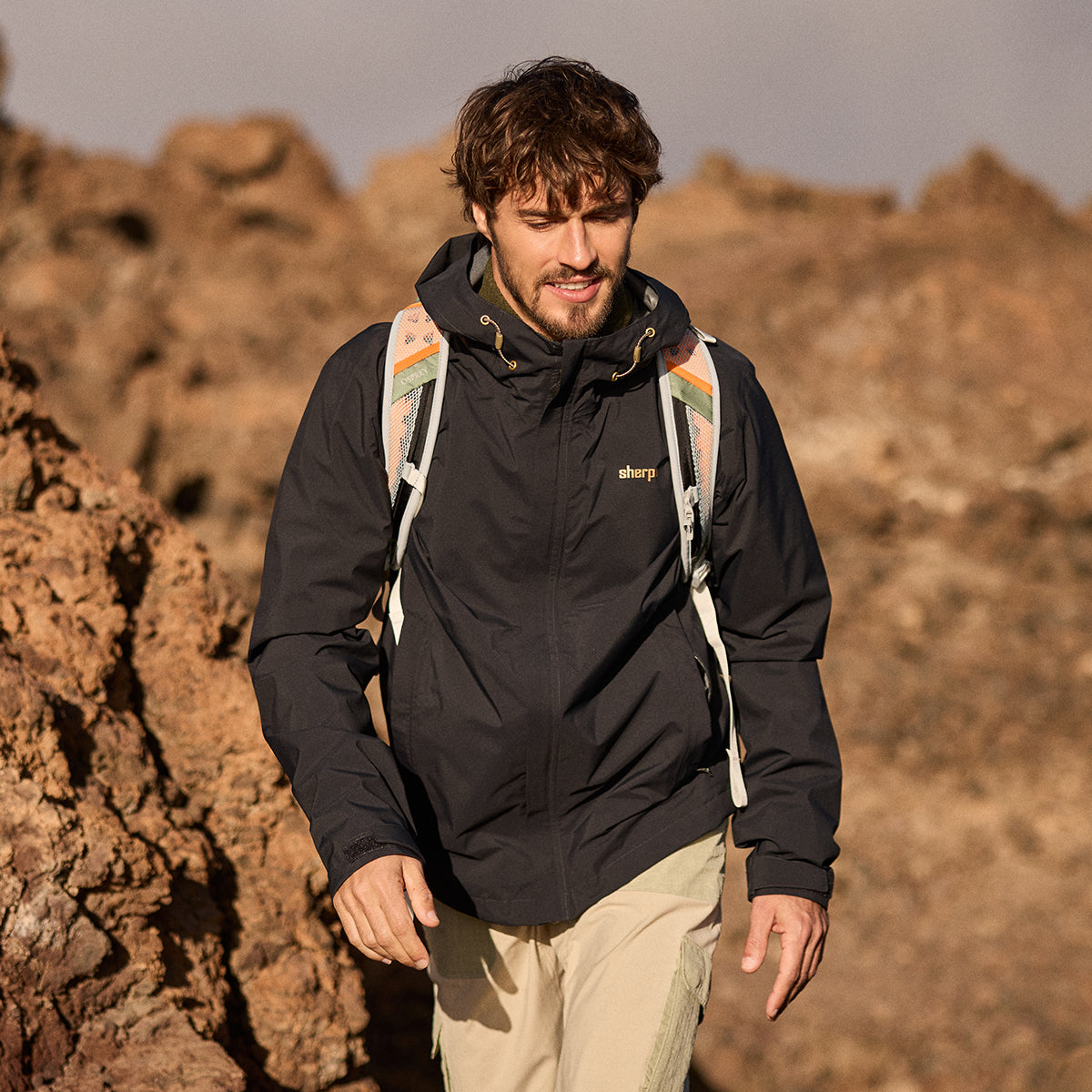Man wearing a black waterproof jacket with a backpack in a rocky desert landscape