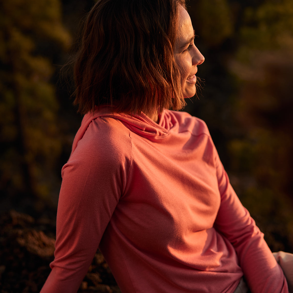 Woman in a lightweight pink hoodie sitting outdoors with a blurred natural background
