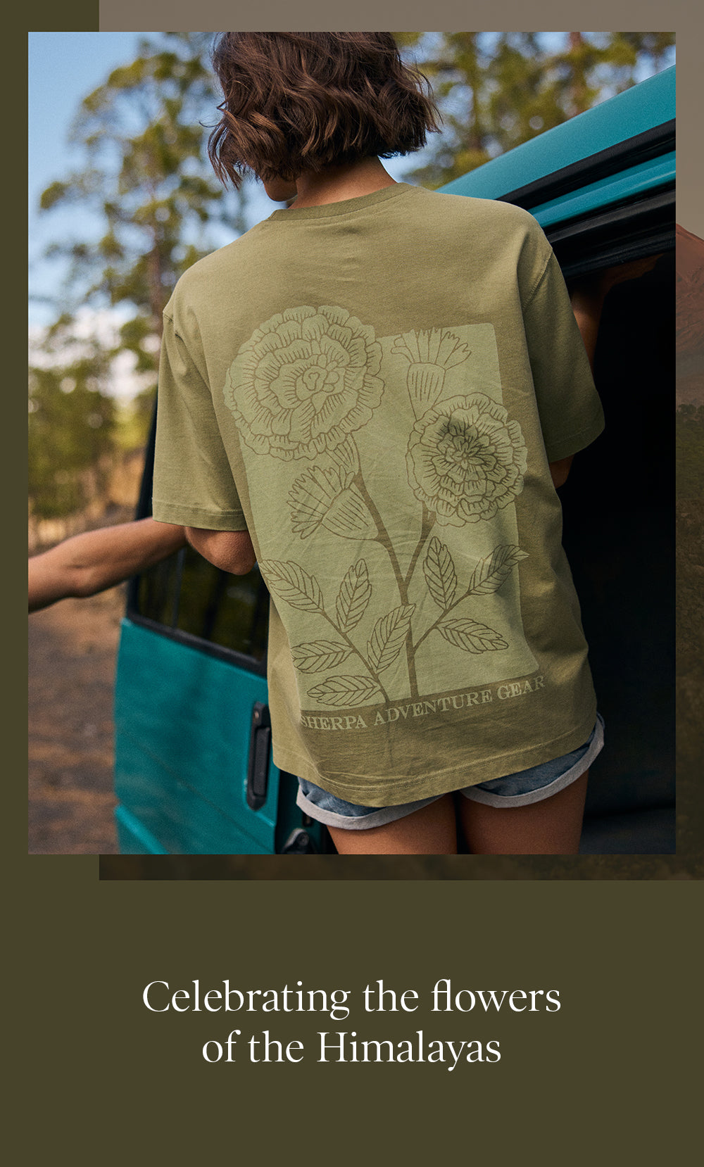 A back view of woman wearing a green t-shirt with floral design outdoors. She is standing next to a blue campervan.