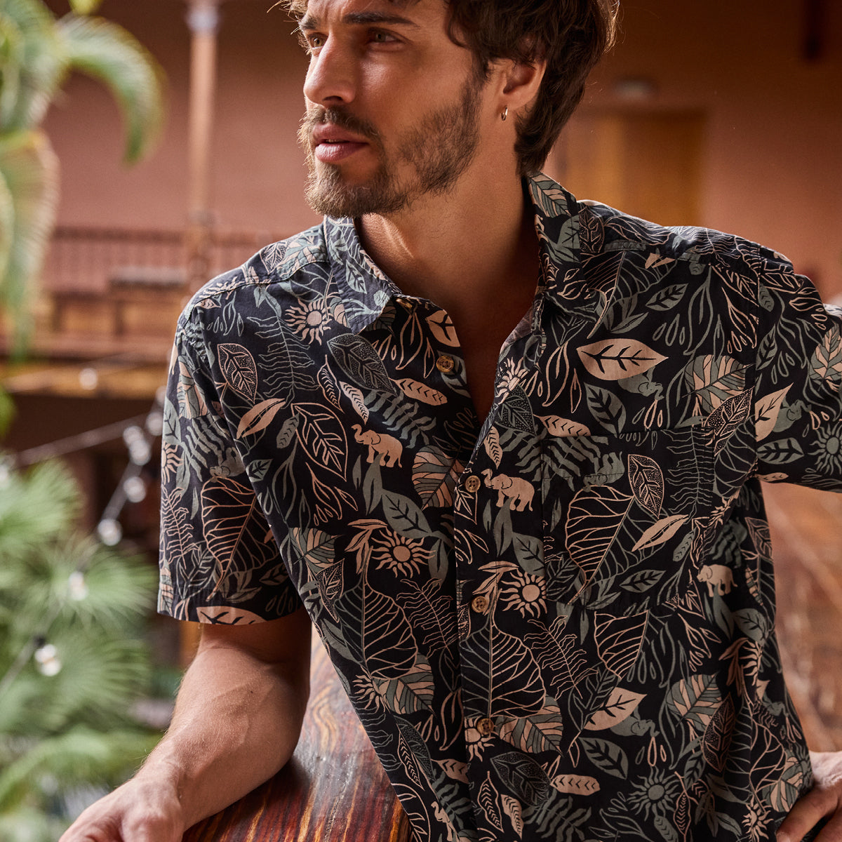 A man wearing a patterned shirt with a Nepal themed design in an indoor setting.