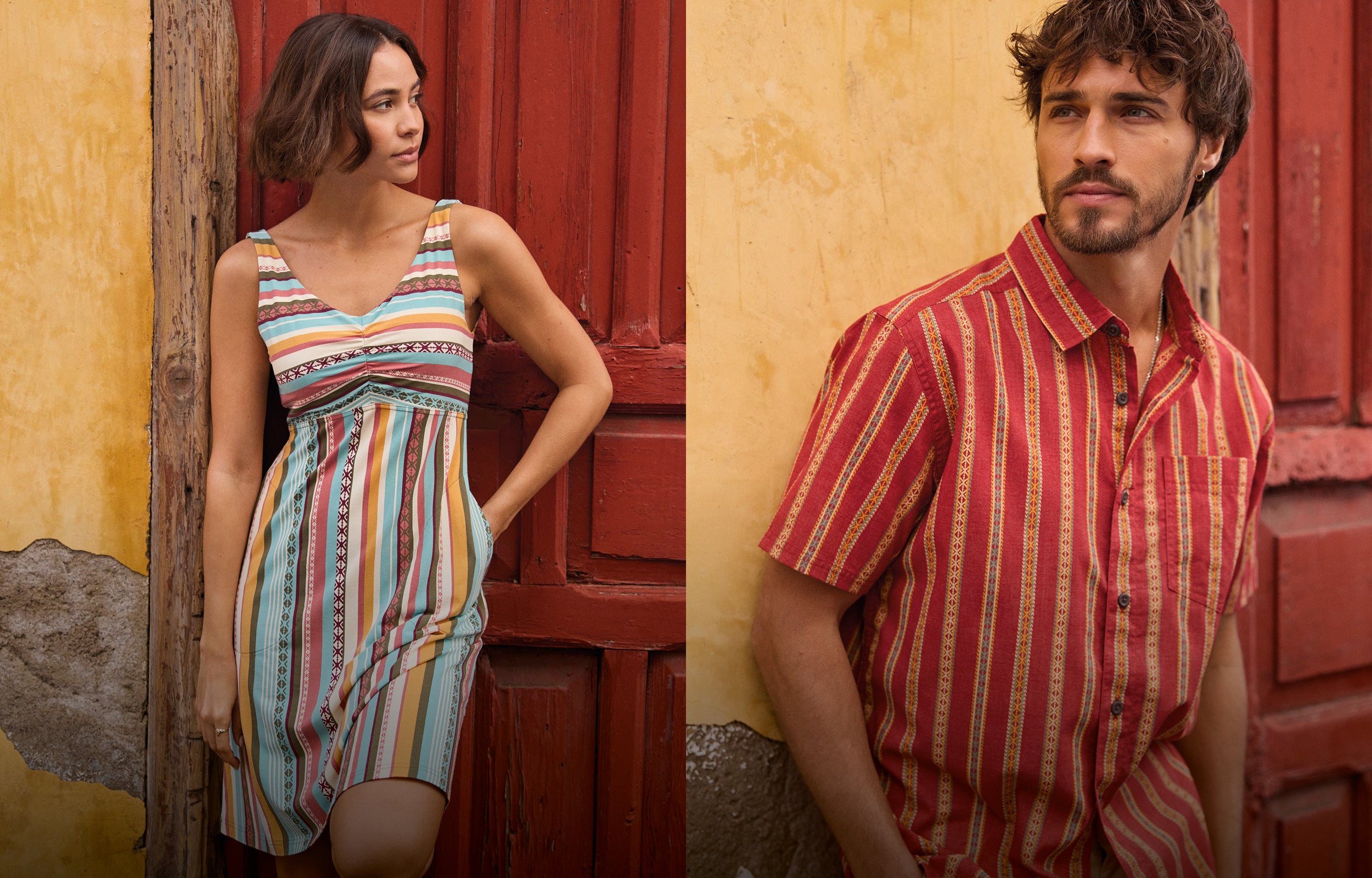 Woman in a colorful dress and man in a red striped shirt against a rustic wall.