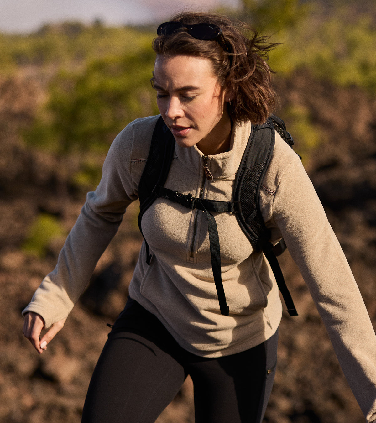 A woman hiking with a backpack on a natural landscape. She is wearing a cream half zip fleece a pair of black leggings.