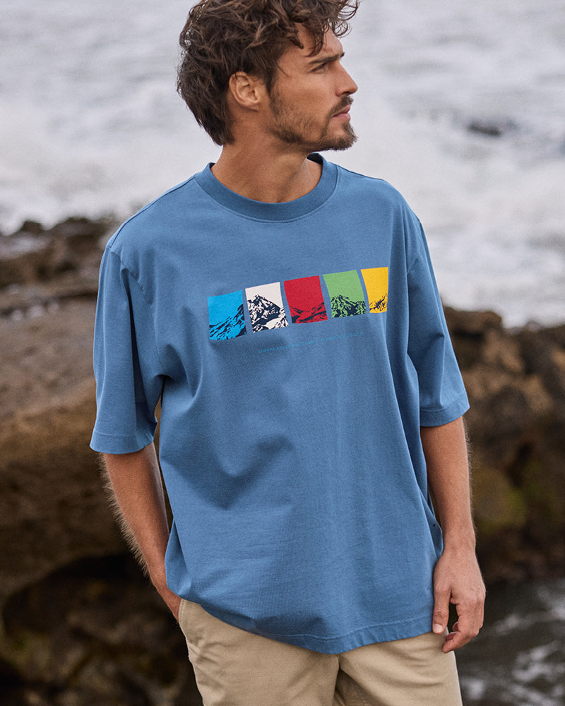 Man wearing a blue t-shirt with colorful mountain design by the water