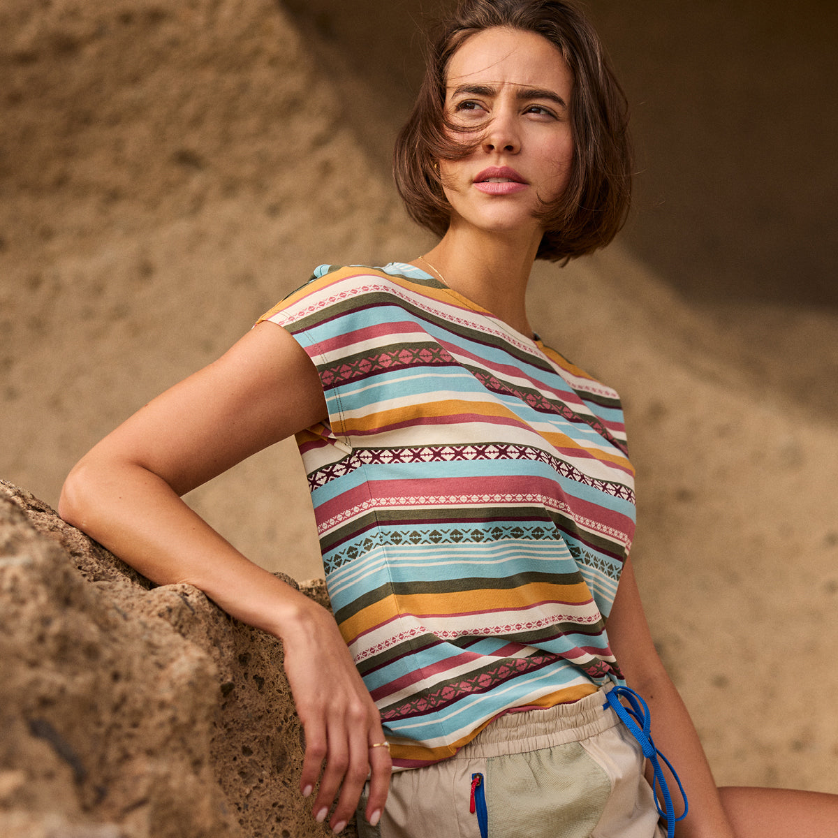 Woman wearing a colorful striped shirt against a textured sandstone wall.