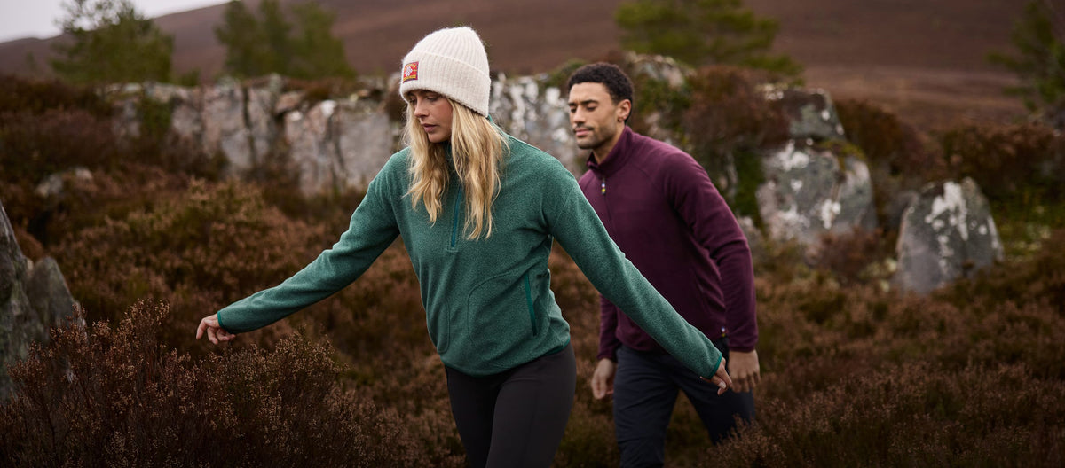 Two people hiking in a heathered landscape, wearing green and burgundy quarter-zip fleeces.