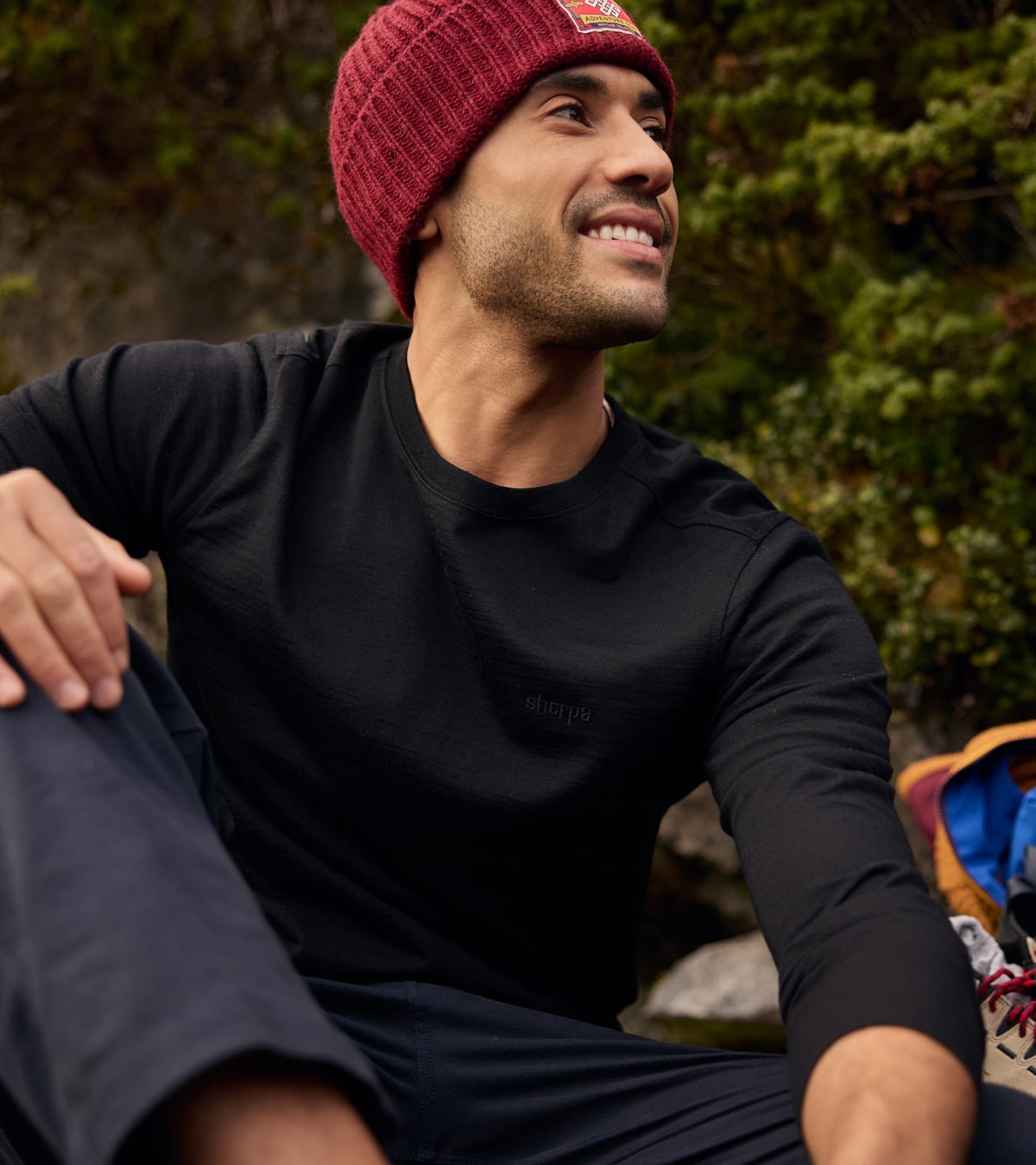 Man in a black long-sleeve shirt and burgundy beanie sitting outdoors.