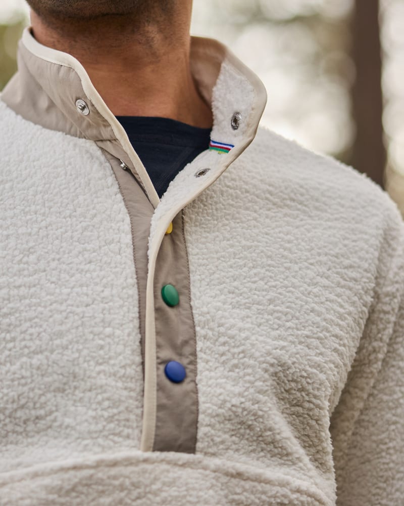 Person in a cream sherpa fleece quarter-zip with colorful buttons, layered over a dark shirt.