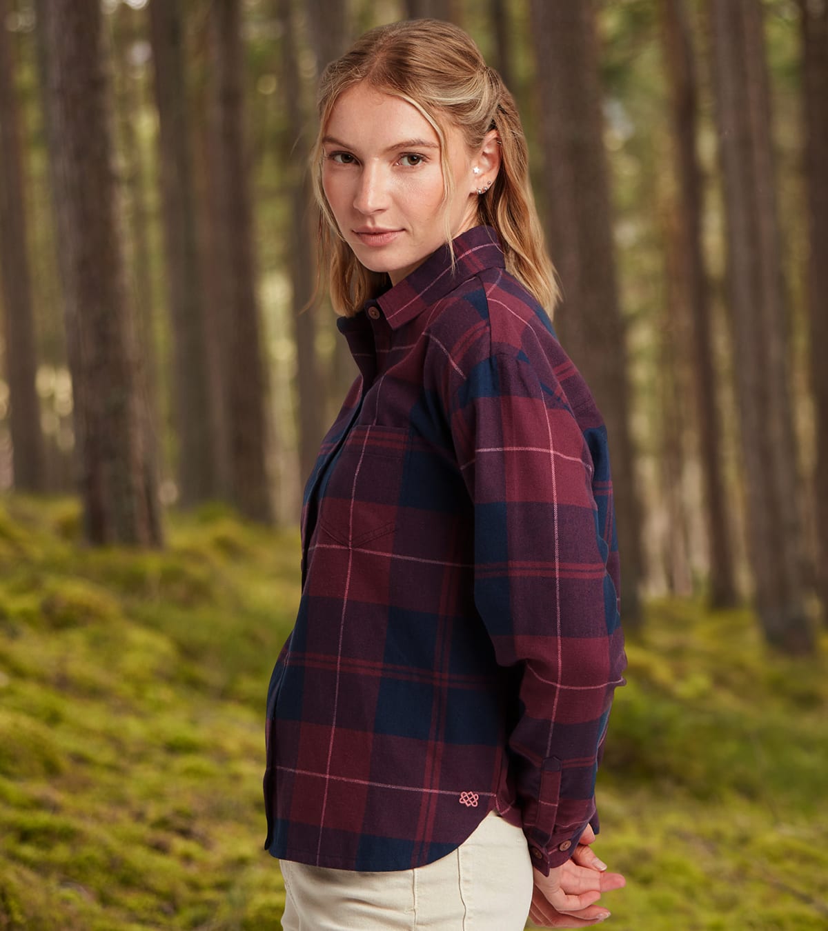 Woman wearing a burgundy and navy plaid long-sleeve shirt, standing in a forest.