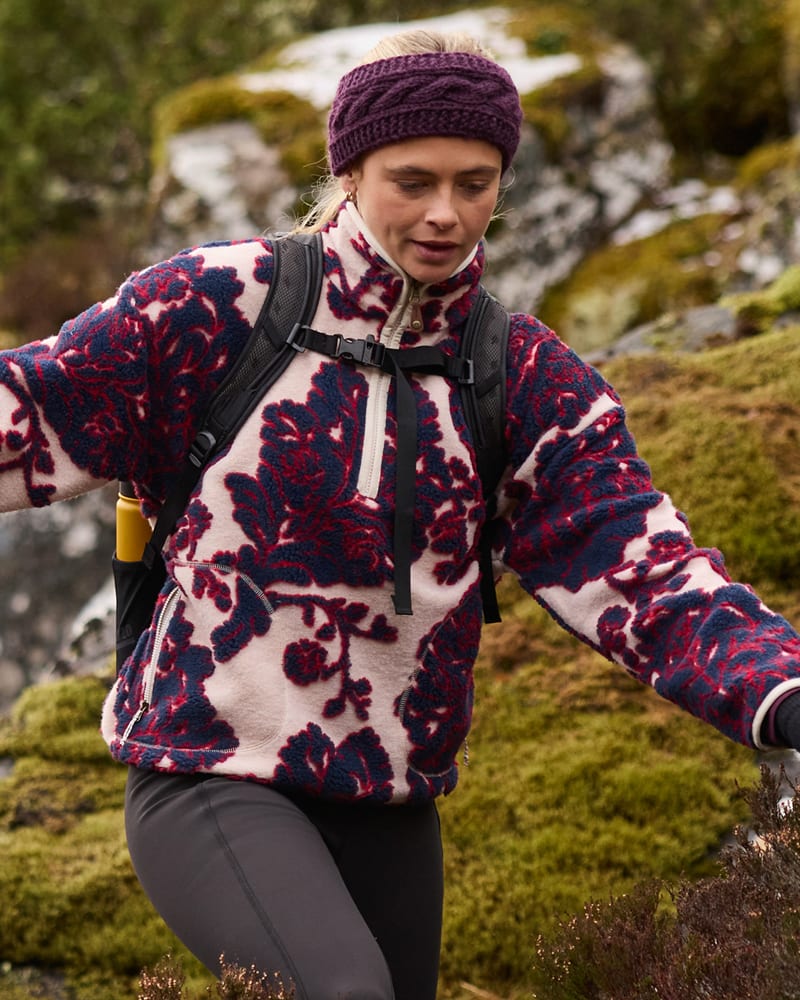 Woman hiking in a cream floral fleece with a purple beanie and black backpack.