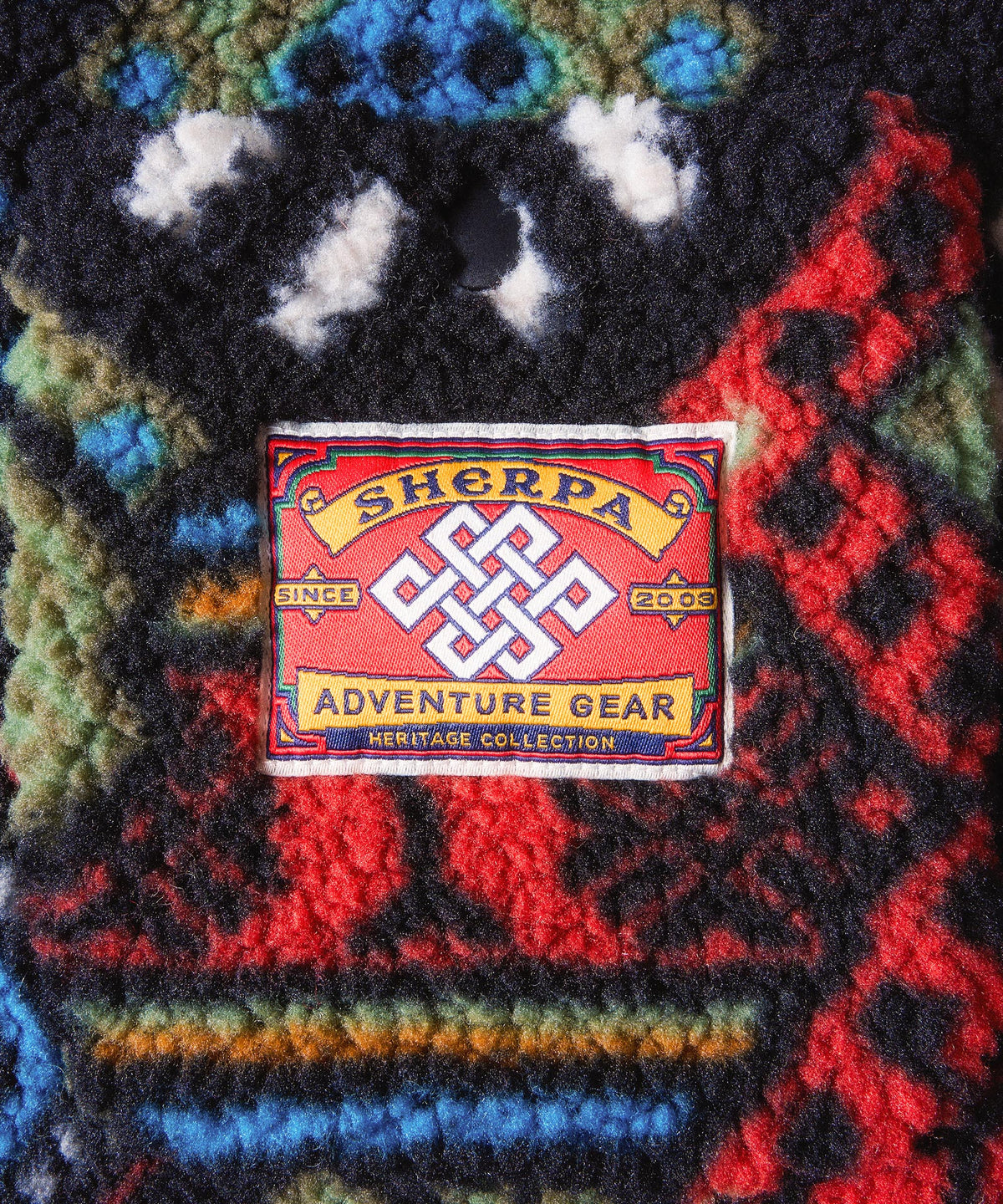 A close-up of a textured sherpa fleece garment featuring a colorful, multicolor Nepal pattern.