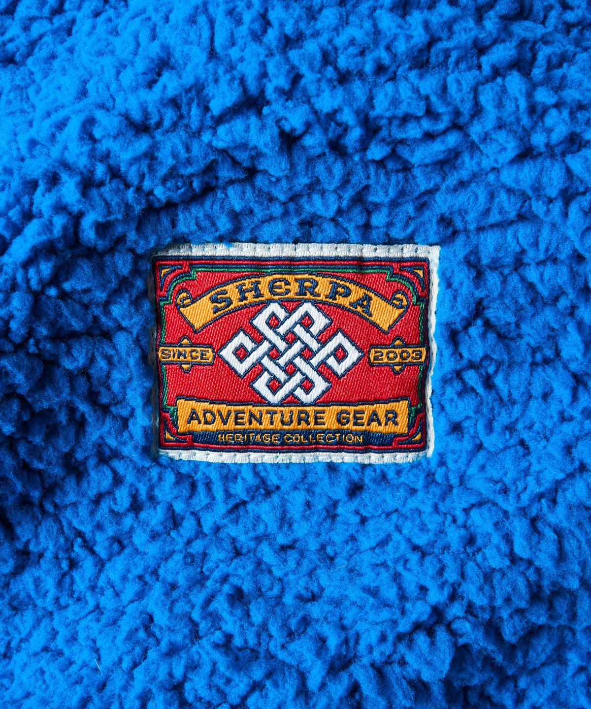 A close-up of a bright blue sherpa fabric with a embroidered Sherpa brand patch in the center.