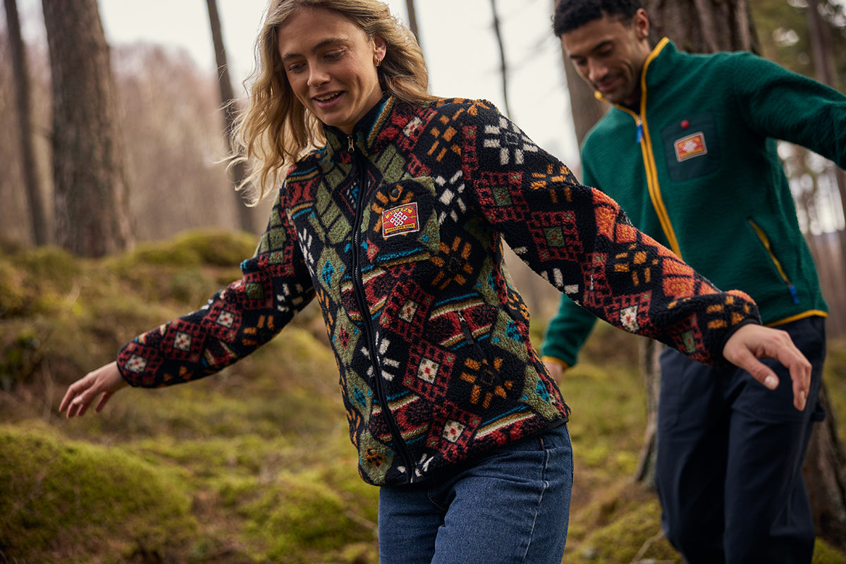 Woman hiking in a forest wearing a colourful patterned fleece, with a man in green fleece behind.