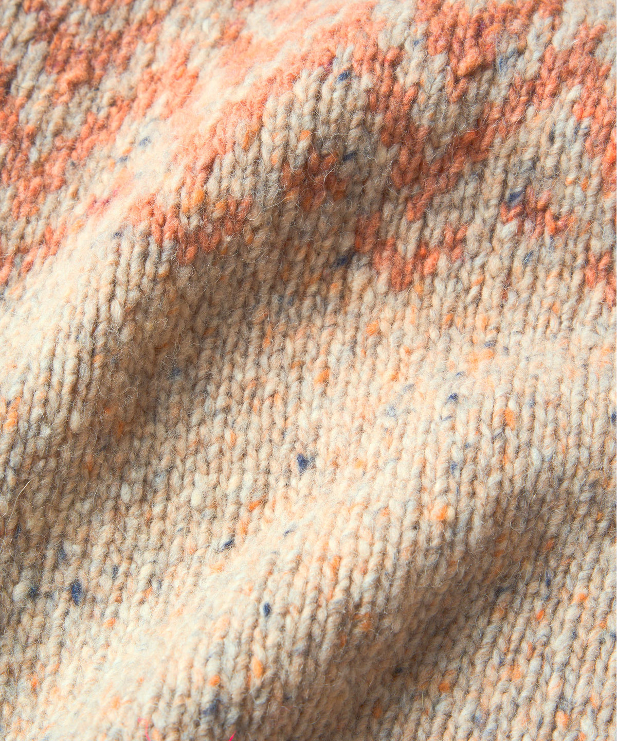 Close-up of a textured knit fabric with a speckled pattern in cream, peach, and blue.