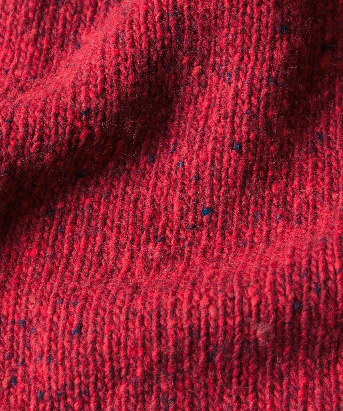 Close-up of a red knit fabric with dark blue and black flecks throughout.