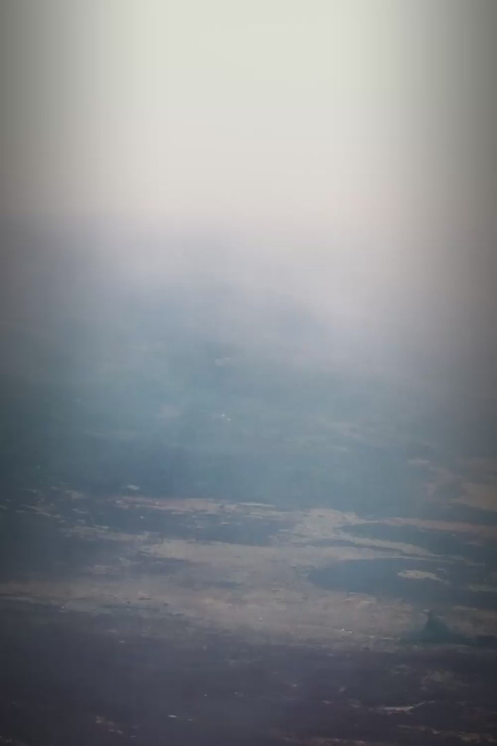 Aerial vertical view of a misty, hazy landscape over mountains and terrain.