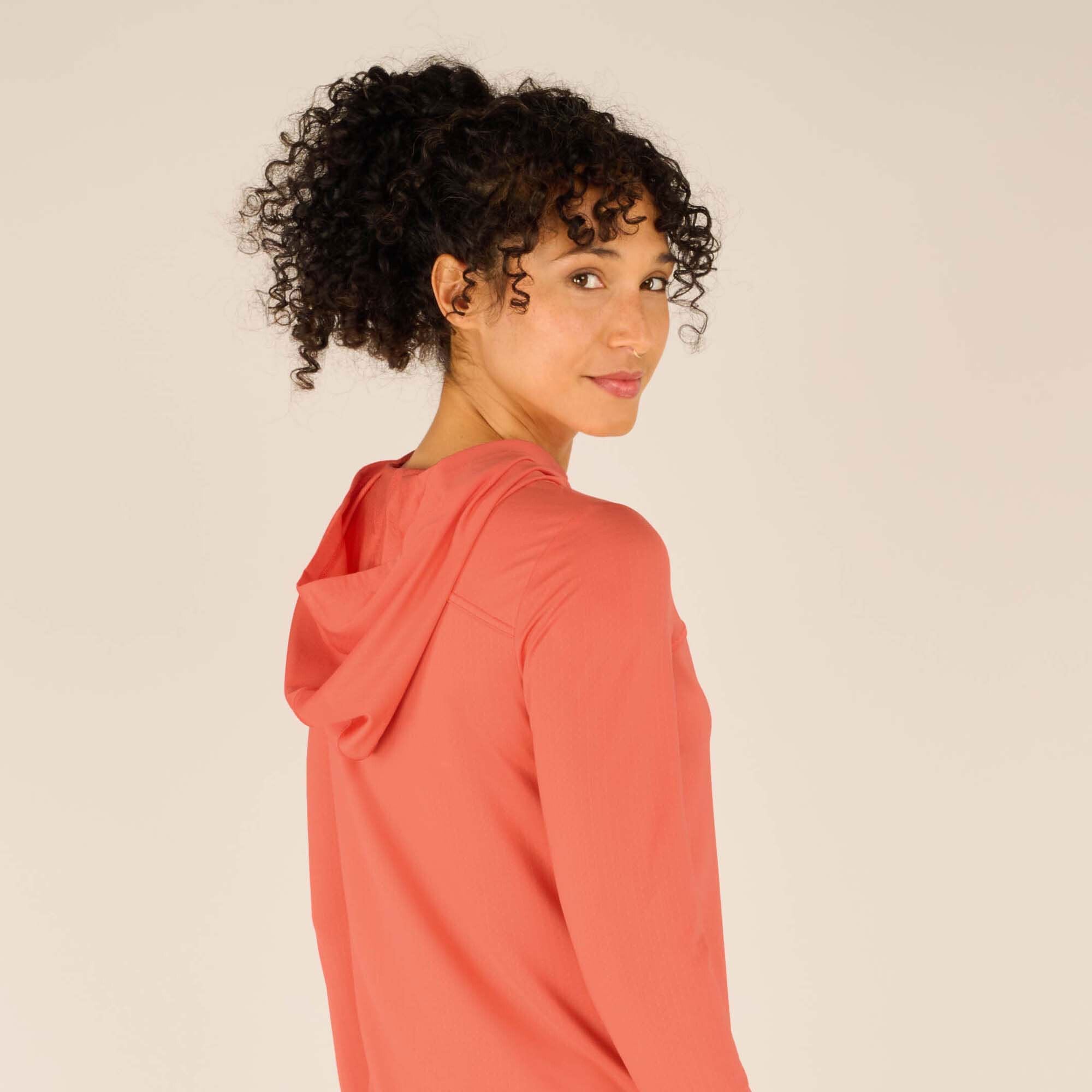 Close-up back view of the woman wearing the Sherpa Adventure Gear Aarti Hoodie in Pink, showing the hood resting flat and smooth on her back. Her curly hair is pulled up, allowing a clear view of the hood’s size and shape.