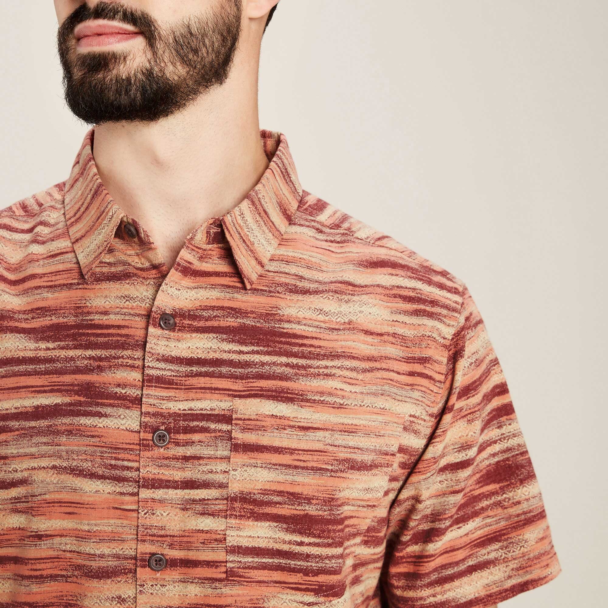 A detailed image focusing on the Sherpa Adventure Gear Khamsu Short Sleeve Shirt in Beige's upper portion. The close-up emphasises the neatly stitched collar, the texture of the beige and red fabric, and the chest pocket with a subtle button detail. This perspective highlights the intricate woven pattern and craftsmanship of the shirt material.