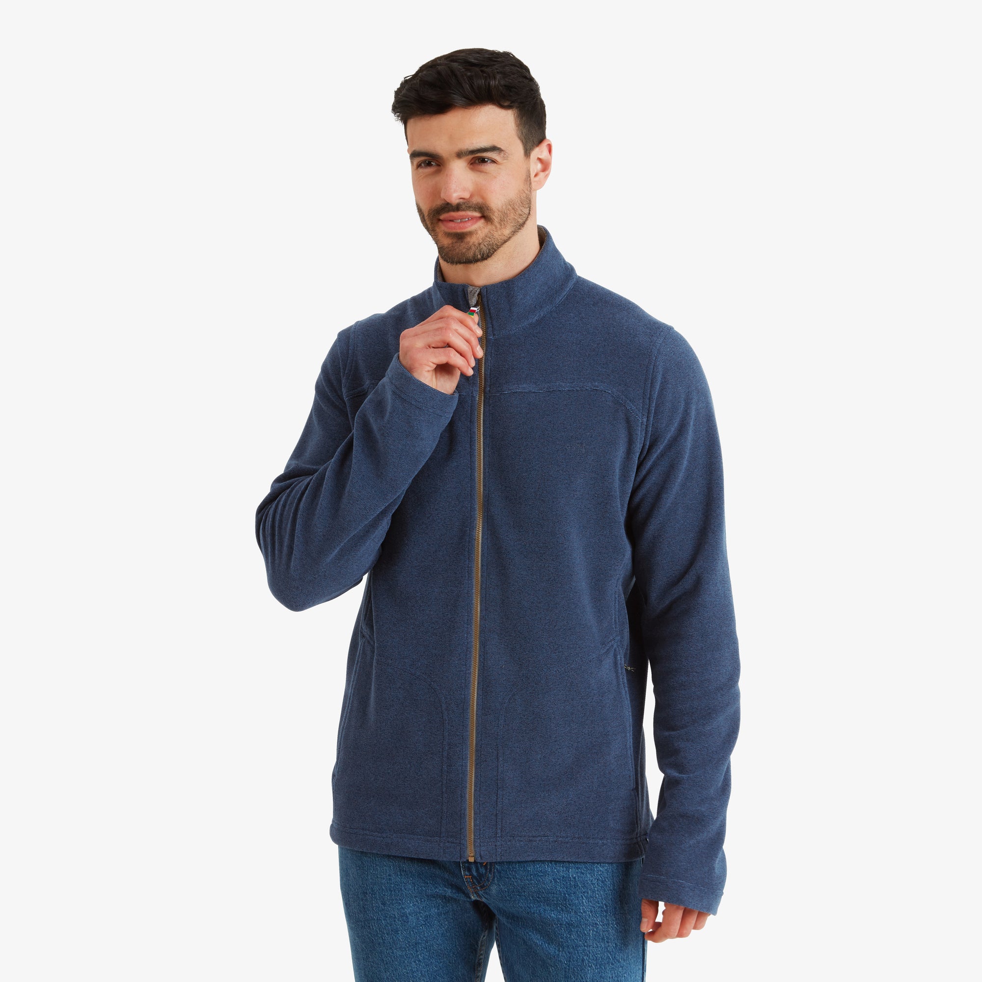 A man is modeling a Sherpa Adventure Gear Rolpa Eco Jacket in Blue. The full-zip jacket features a clean front design with subtle stitch detailing. He is holding the zipper lightly near his neck, showcasing the zipper's functionality and highlighting the soft collar.