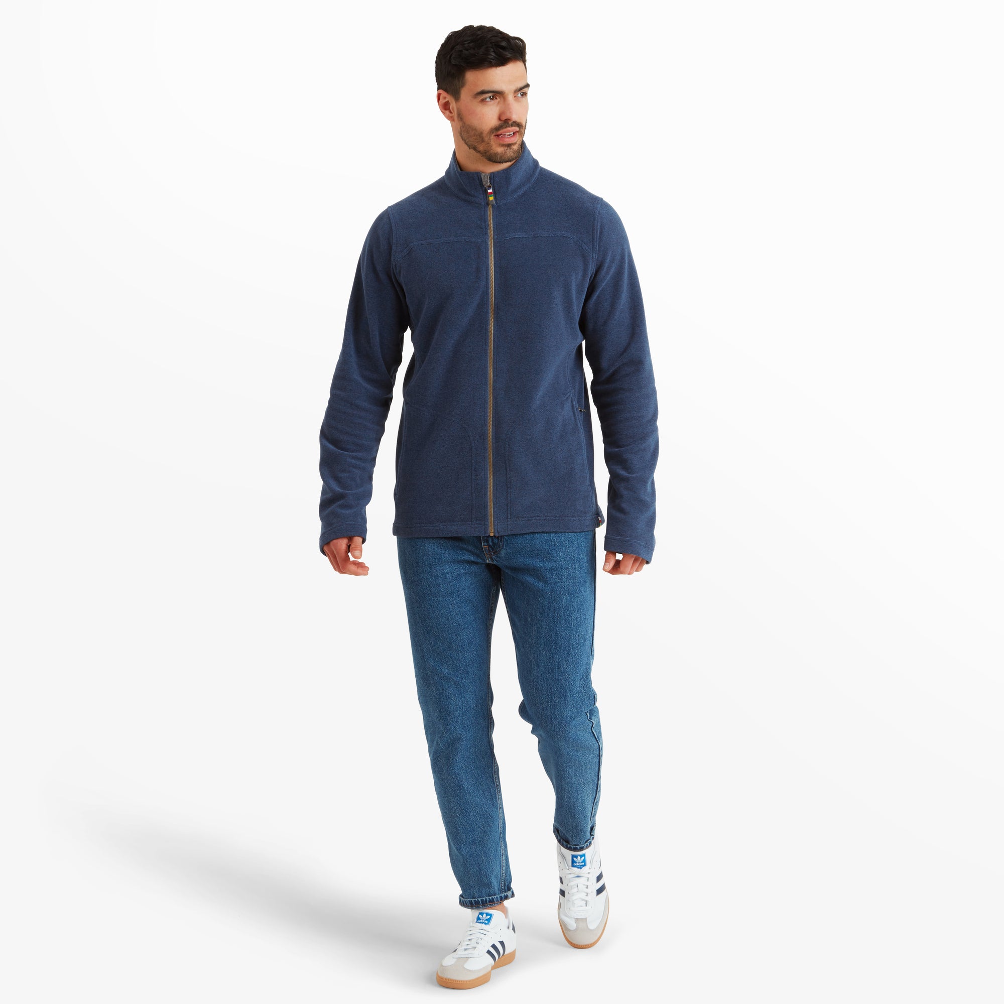 The model is seen walking forward while wearing the Sherpa Adventure Gear Rolpa Eco Jacket in Blue. The midweight material is displayed in a casual style paired with denim jeans and white trainers. The straight-cut fit and relaxed look of the jacket are emphasised.