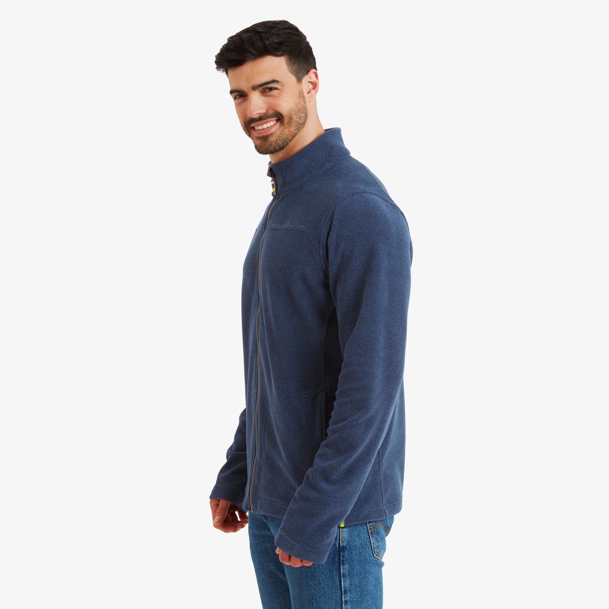 The model is turned slightly to the side, displaying the slim and functional cut of the Sherpa Adventure Gear Rolpa Eco Jacket in Blue. The zippered side pockets are visible, showing practical storage options. The collar sits neatly against his neck, giving a refined yet casual look.
