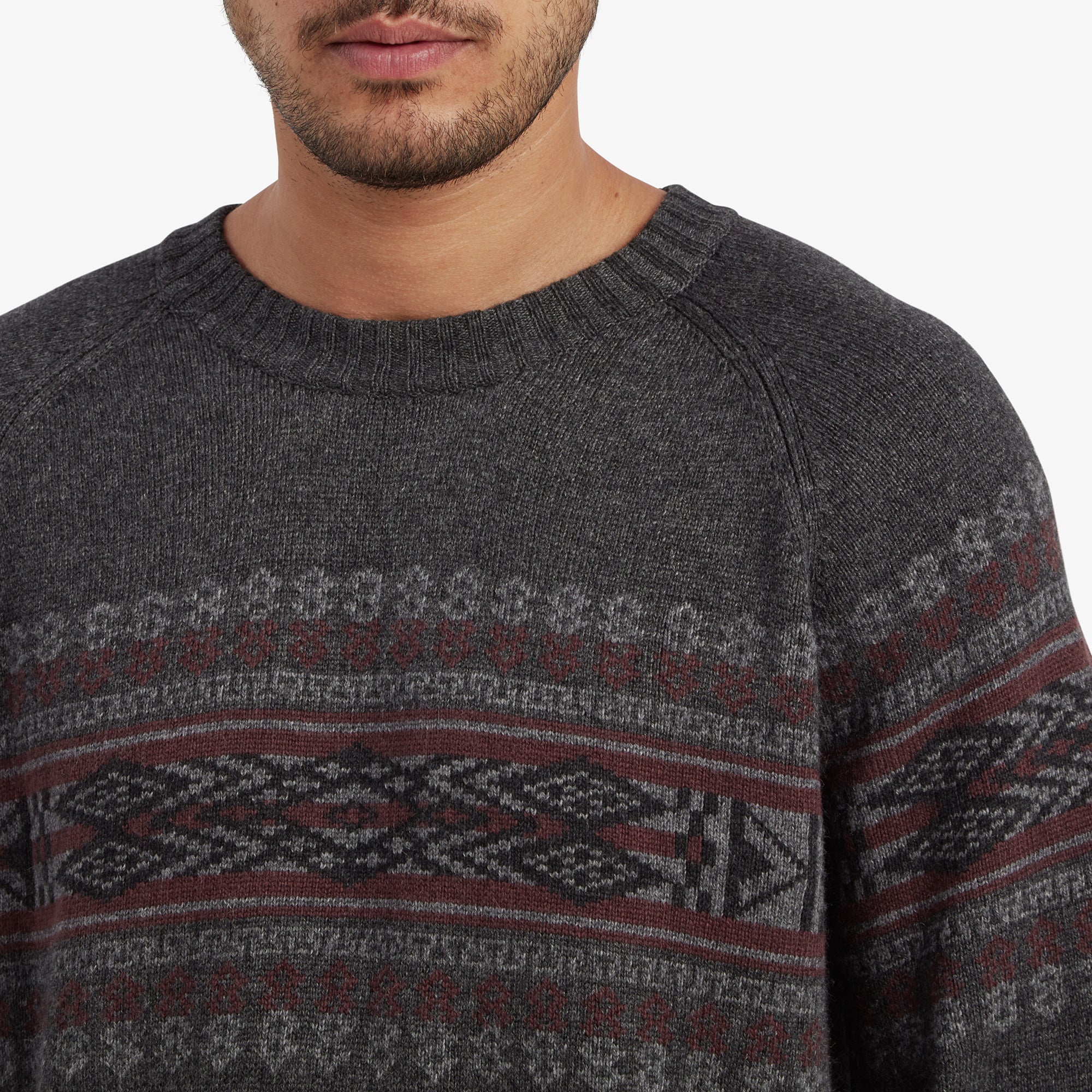 A close-up shot focusing on the intricate pattern on the Sherpa Adventure Gear Sajit Eco Crew in Grey's chest area, featuring traditional motifs in red and grey against the dark grey background. The fine-knit texture of the fabric is clearly visible.