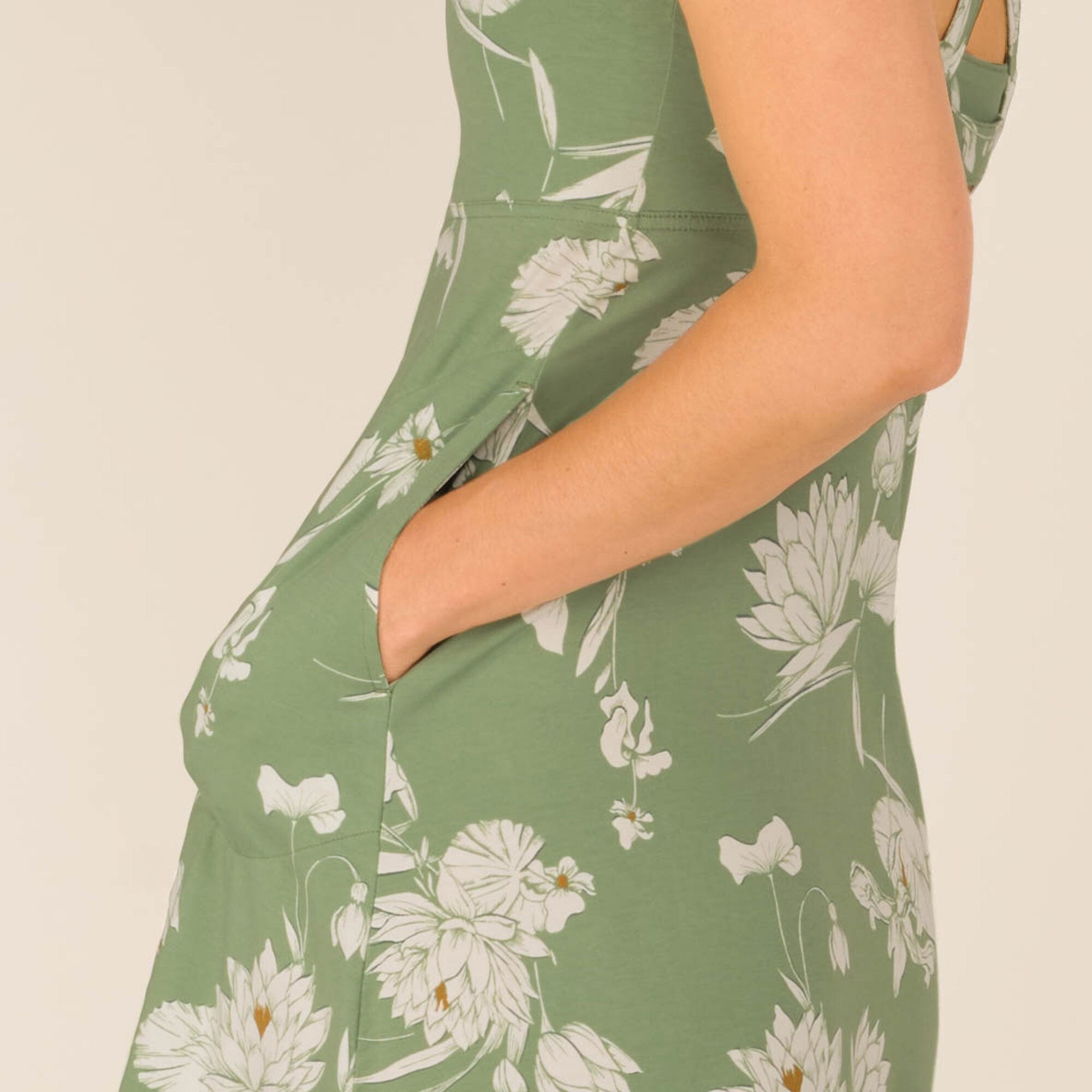 A close-up shot of the Sherpa Adventure Gear Neha Dress in Green’s pocket detail, showing a woman’s hand slipping into a discreet side pocket. The white floral design contrasts against the green fabric, emphasizing the dress's functionality and stylish appeal.