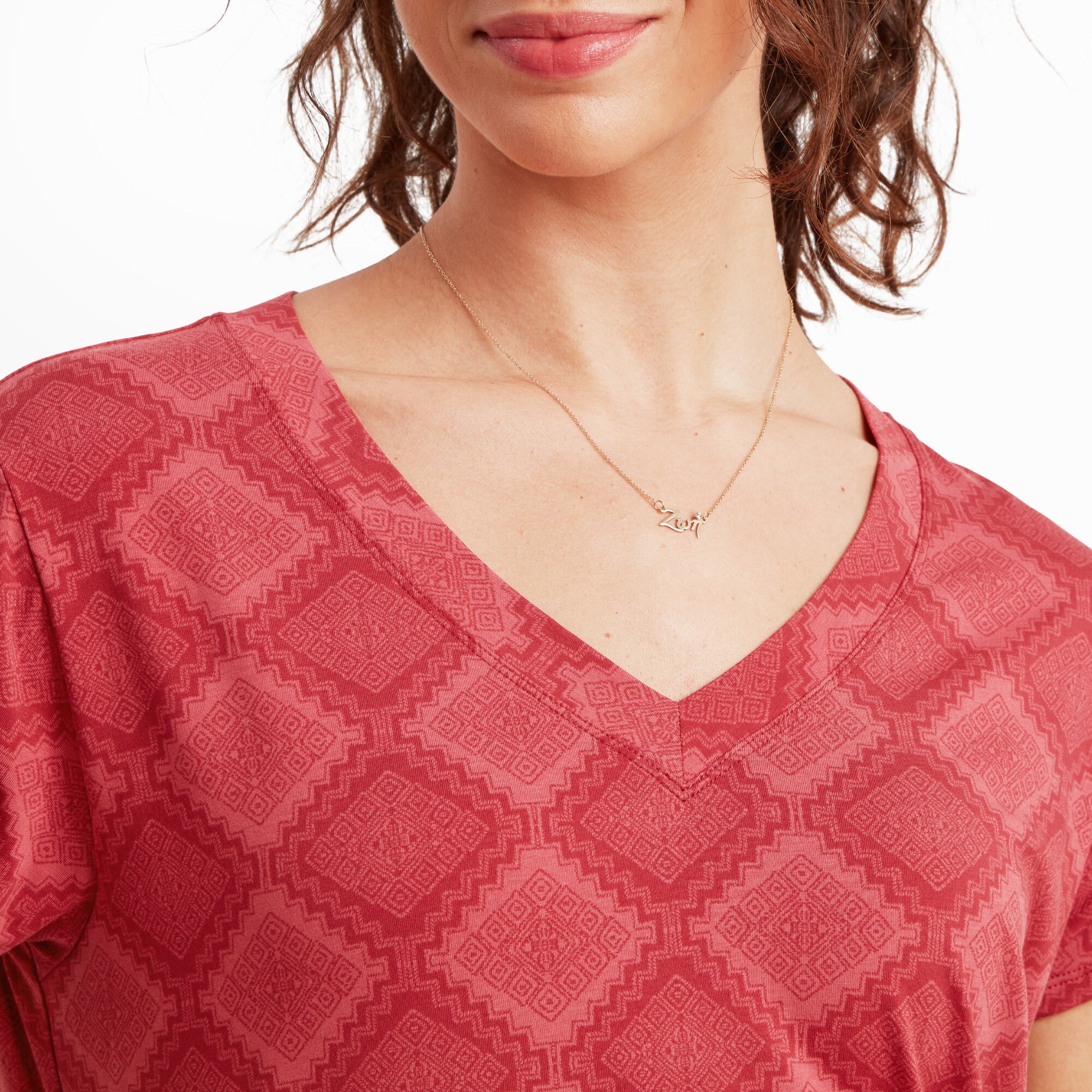 A close-up of the Sherpa Adventure Gear Neha V-Neck T-Shirt in Red’s V-neck area, showing intricate geometric patterns in the fabric. A delicate gold necklace with a small charm is also visible on the model’s neck, adding to the details of the look.
