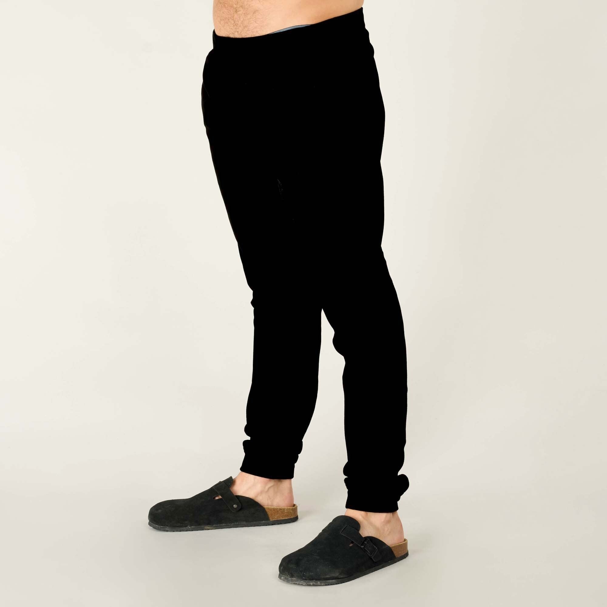 Another side view, captured from the opposite angle, showing the Sherpa Adventure Gear Rolpa Jogger in Black. The side seam and tapered cut are visible, and the fabric appears soft and plush. The person’s feet remain in black suede clogs.