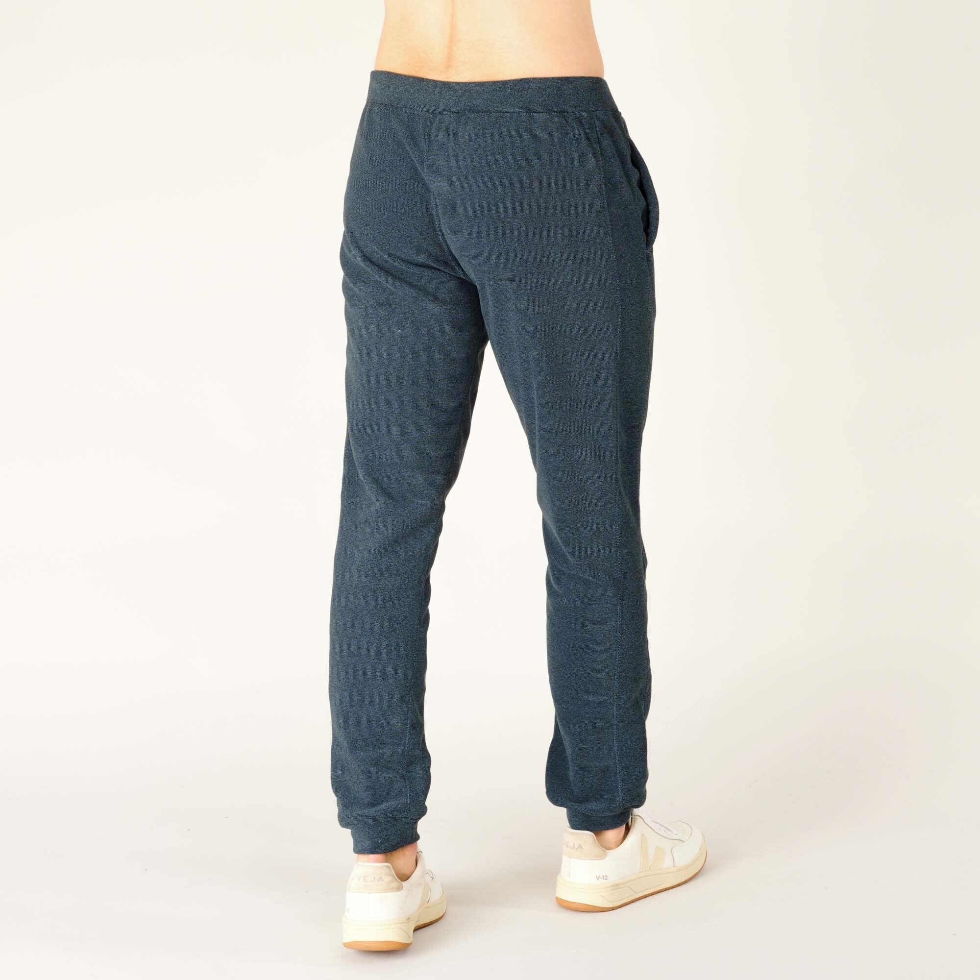 Rear view with the model standing in a relaxed pose, highlighting the simple construction, elastic waistband, and smooth drape of the Sherpa Adventure Gear Rolpa Jogger in Blue.