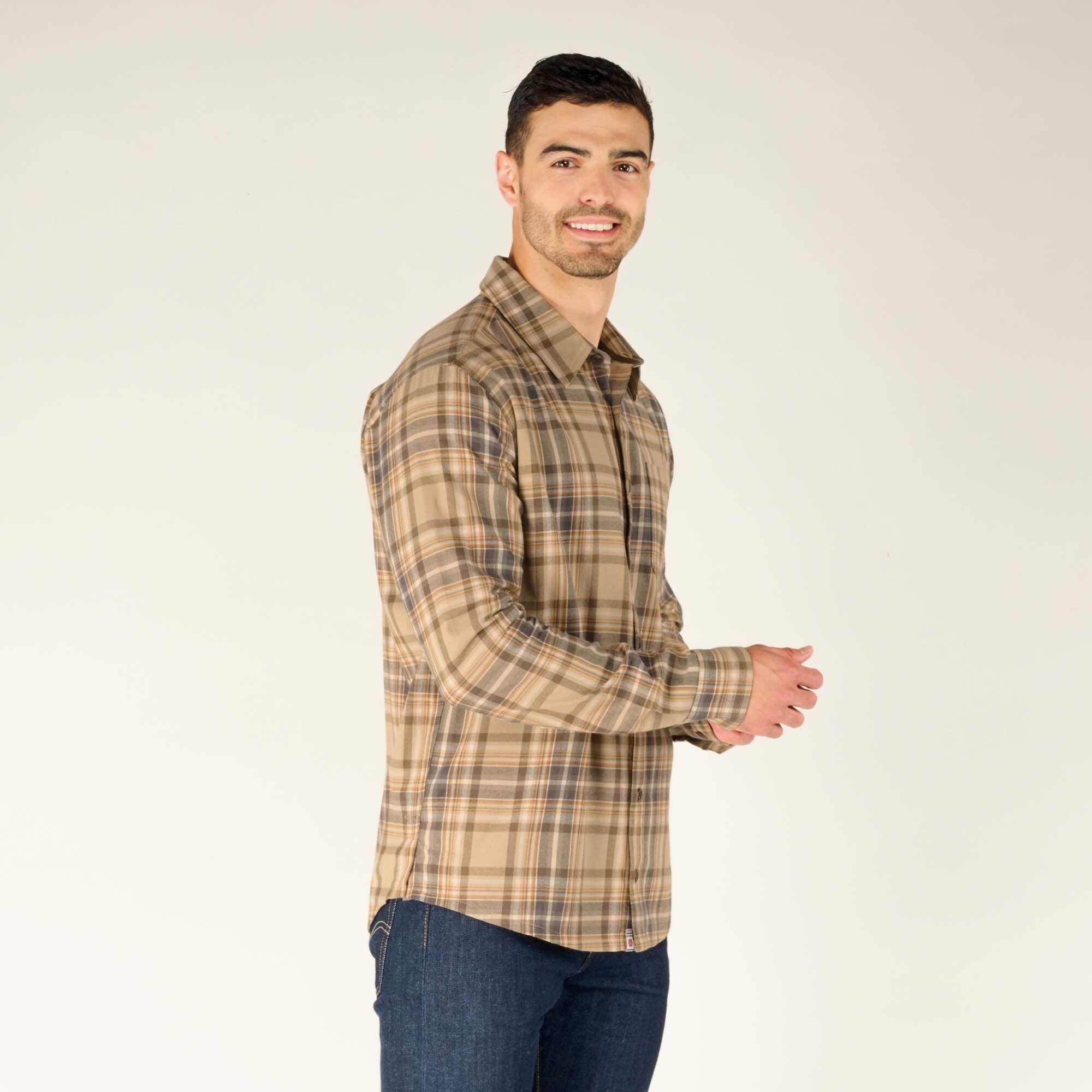 The model is turned slightly to his right, showcasing the side of the Sherpa Adventure Gear Rudra Shirt in Beige. His hands are clasped in front, and he maintains a warm expression. The plaid pattern is evenly distributed, and the side seams are visible.