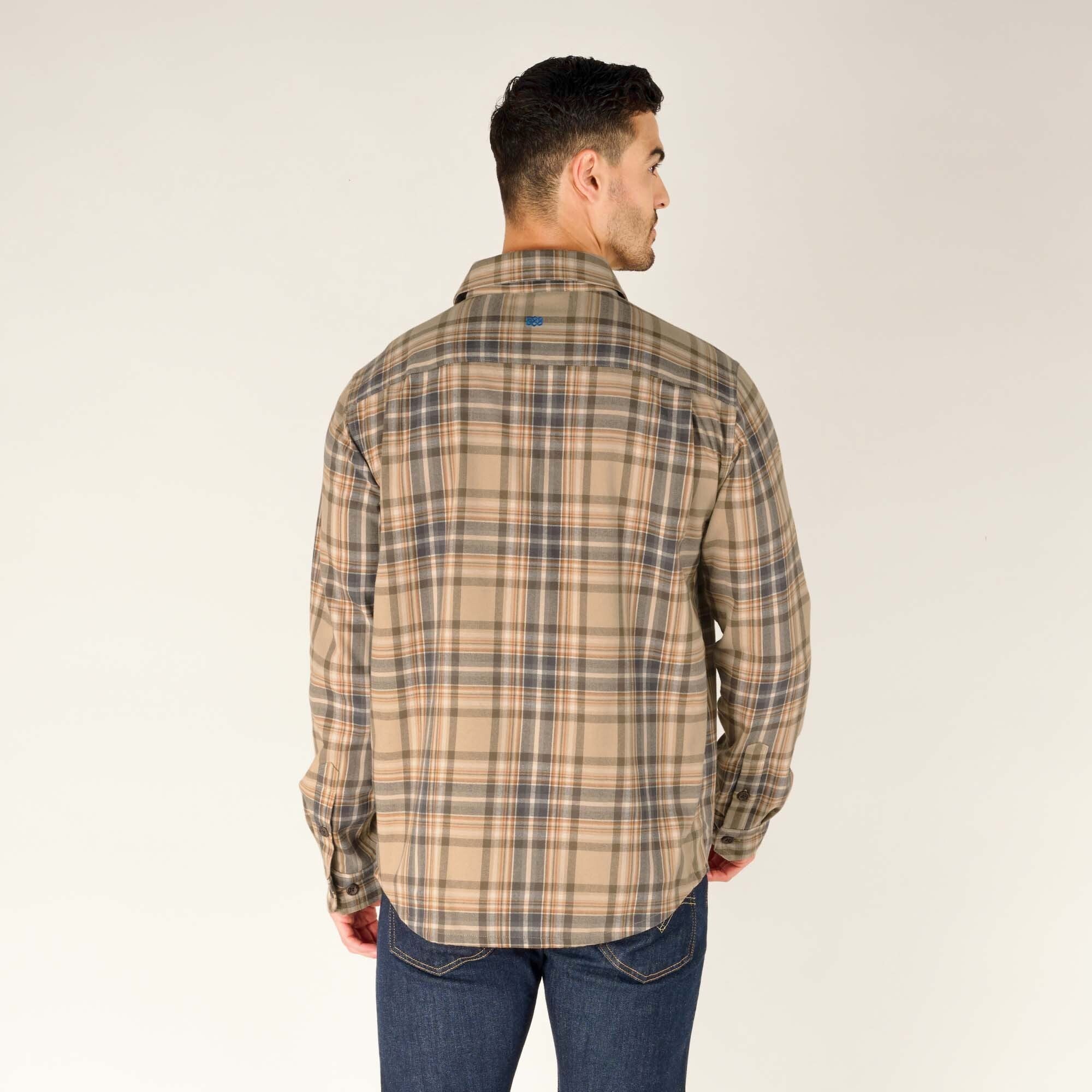 The model is facing away from the camera, showing the full back of the Sherpa Adventure Gear Rudra Shirt in Beige. The shirt's pattern continues consistently across the back, with a slight curve at the hem. The top back of the shirt features a small embroidered blue logo.