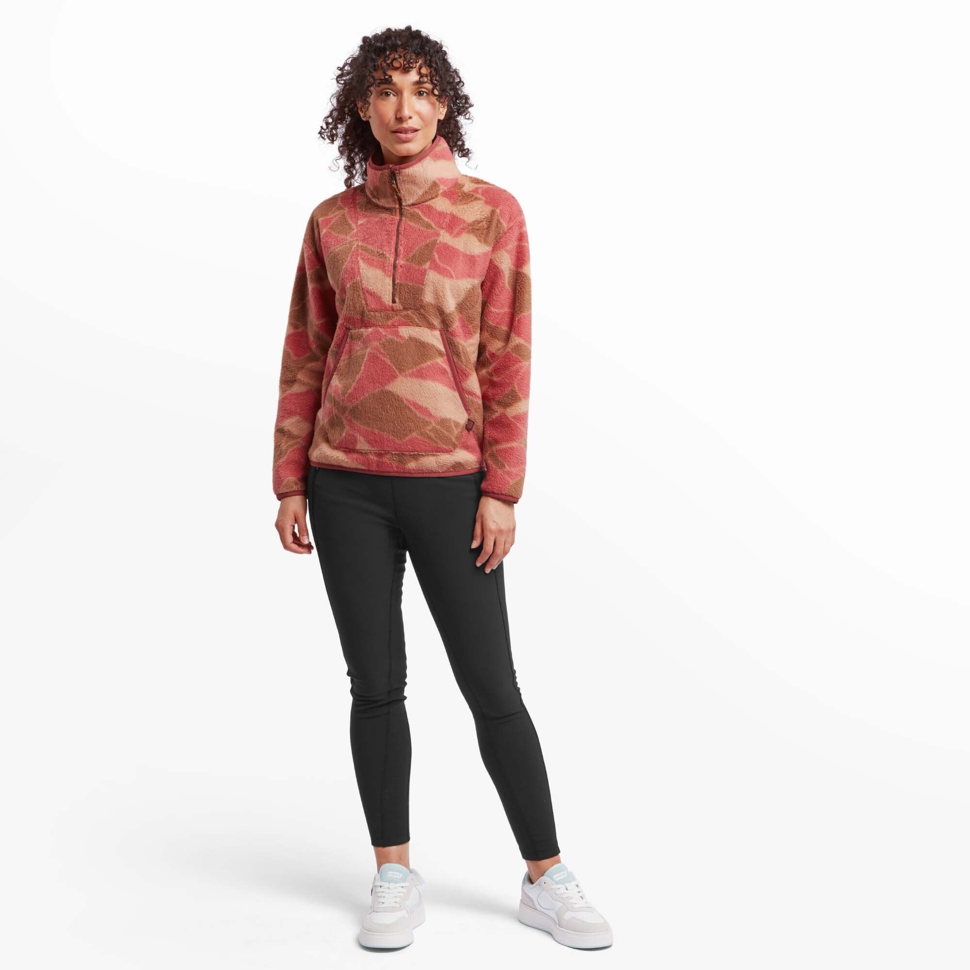 The model is in a relaxed pose, slightly turned with his hands gently resting together in front of him. The Sherpa Adventure Gear Uddesya Eco Quarter Zip in Red drapes naturally over his frame, showing its flexibility and fit. The fabric's subtle heathered texture is visible, and the collar maintains a structured look. The white background keeps the focus on the pullover and its design elements.