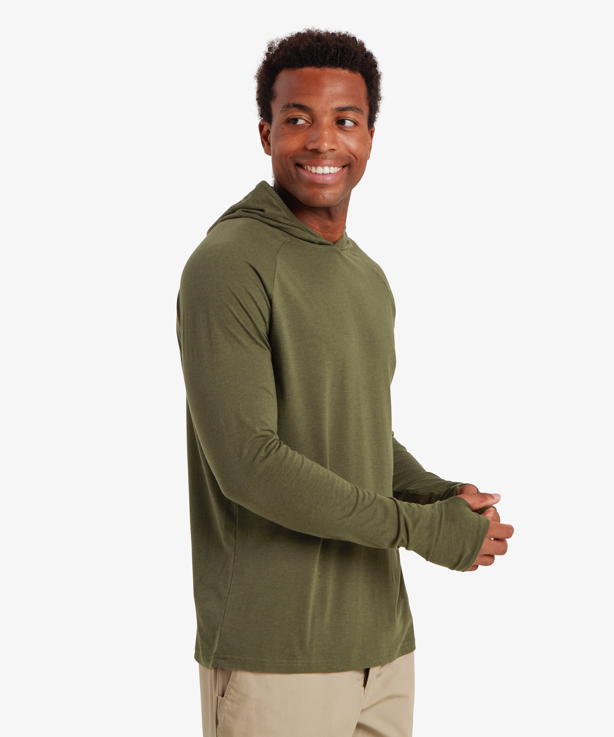 A man wearing a green hoodie with long cuffs and thumb loops. The hoodie is paired with beige walking pants with a pocket on the side. The man is smiling, with his body tilted to the left whilst adjusting the sleeves and thumb loops of his right hand. The outfit is suitable for outdoor activities such as hiking and walking in the summer.