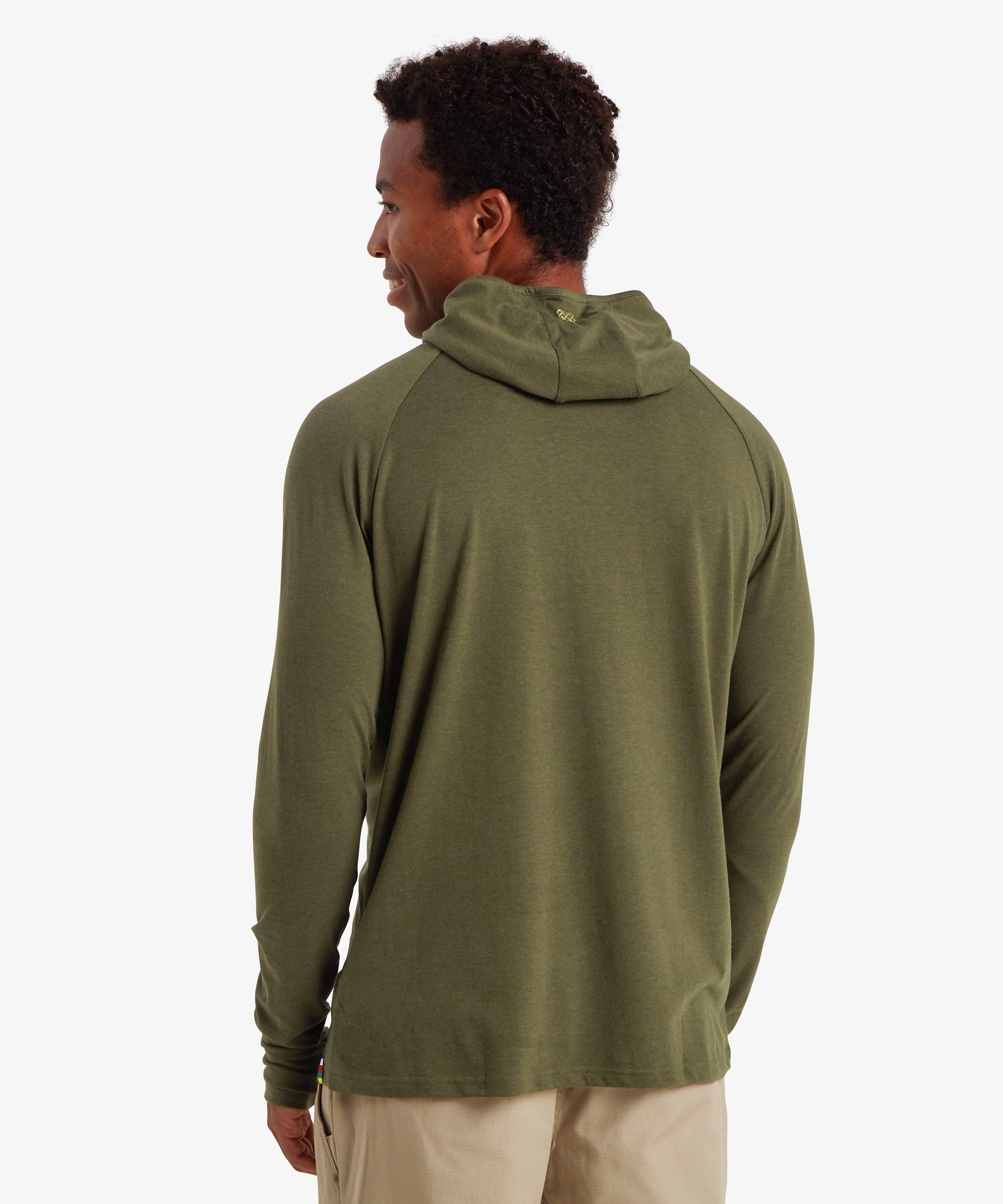 Man viewed from the back wearing a long sleeve, green hoodie with a pair of beige walking pants with a pocket on the side. The hoodie features a small, gold "endless knot" printed logo on the edge of the hood. The man has black curly hair and is standing with his hands down by his sides.