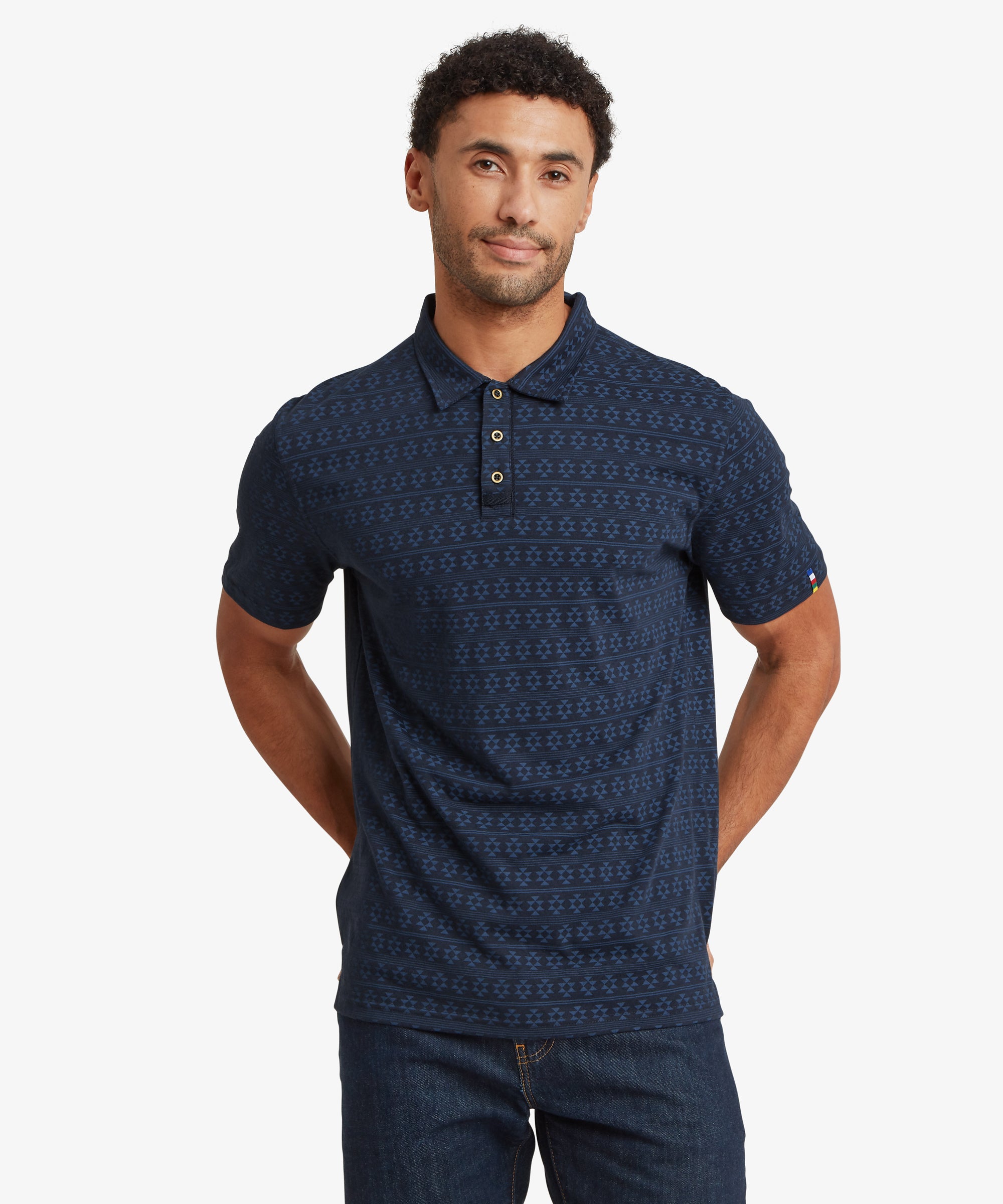 Front view of a navy short‑sleeve polo shirt featuring a repeating geometric pattern and a three‑button placket, paired with dark jeans.
