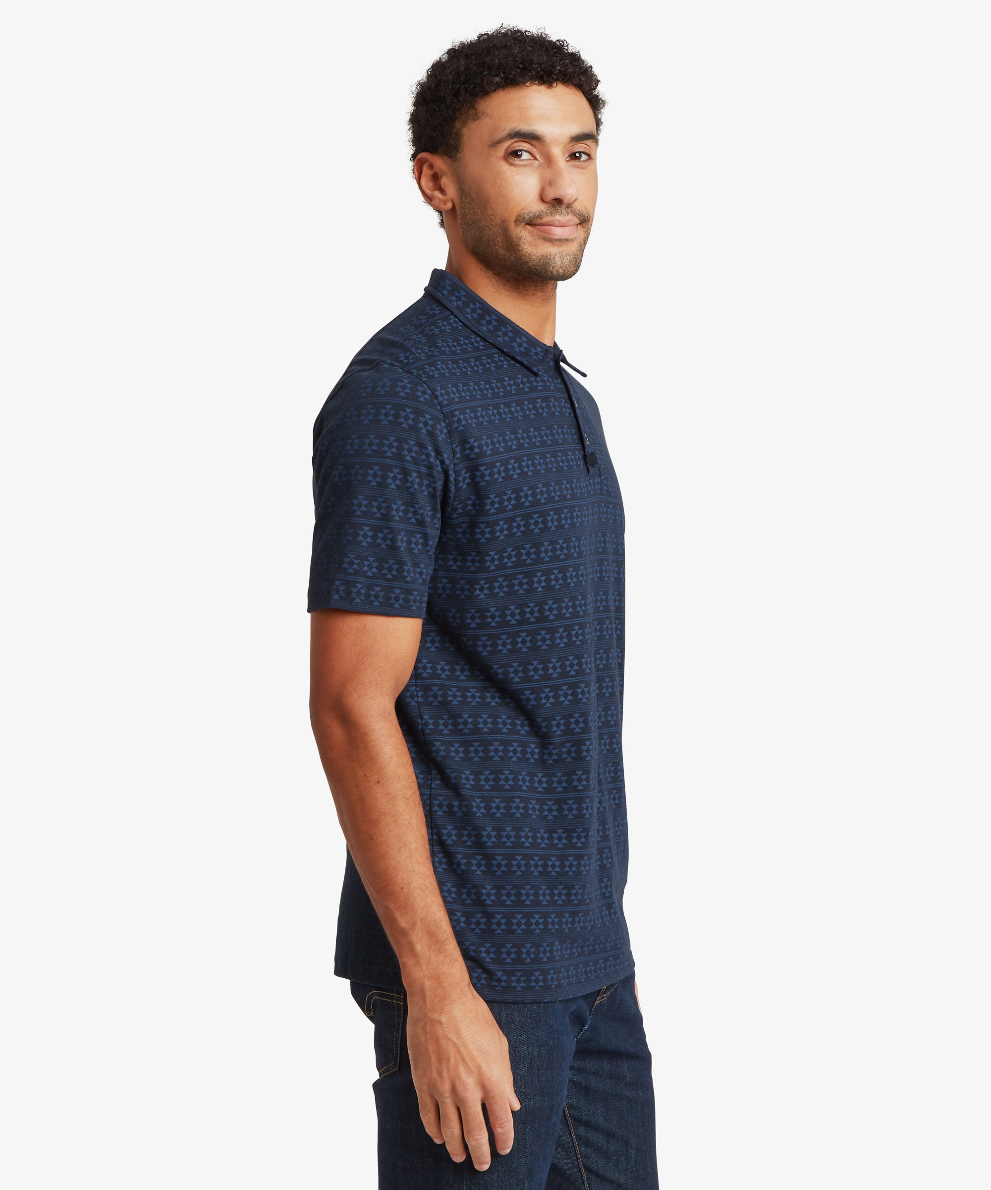 Side profile of a navy geometric‑patterned polo shirt worn with dark denim jeans. The shirt has a structured collar and a subtle all‑over print.