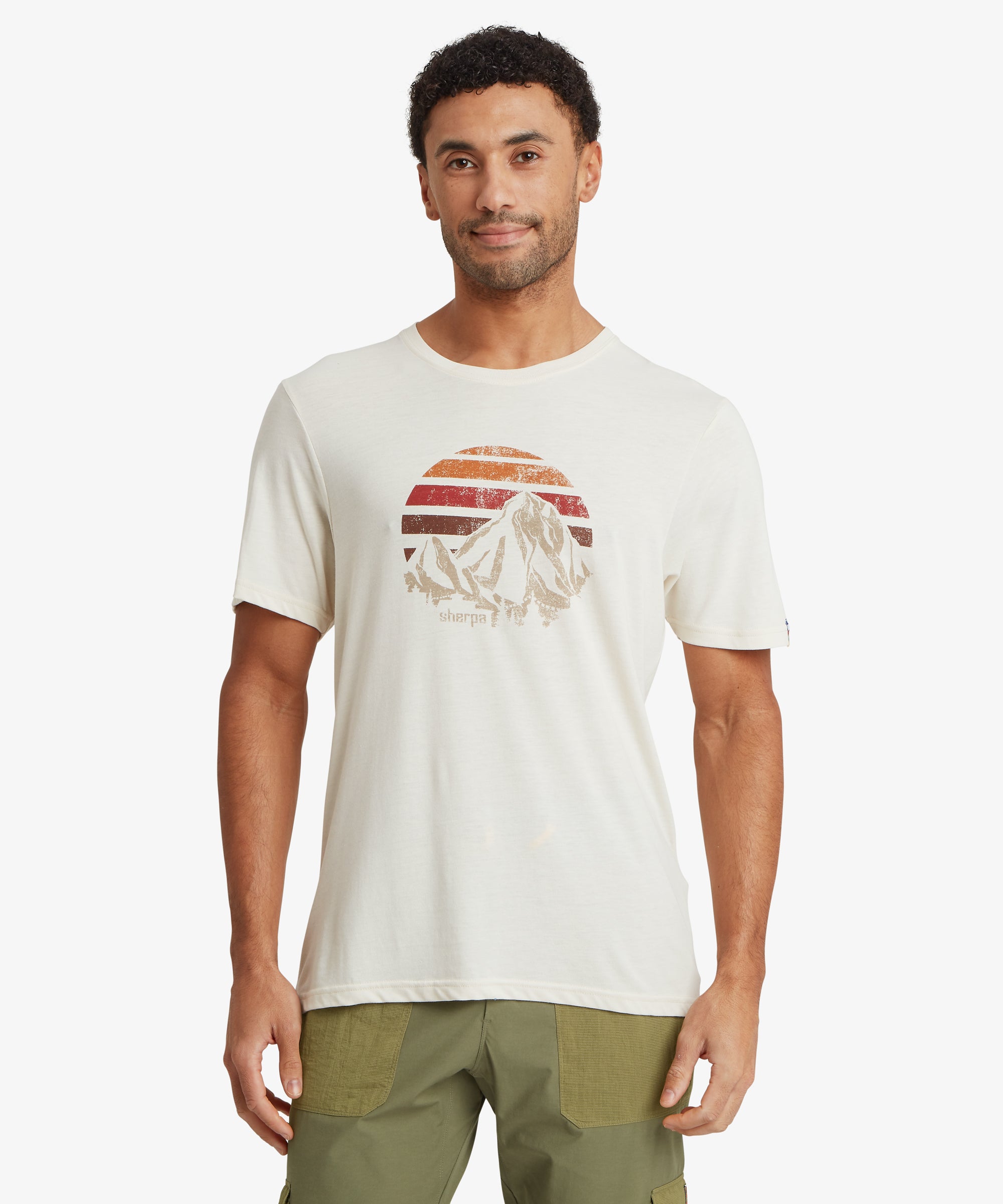 Front view of an off‑white T‑shirt with a distressed mountain graphic inside a circular sunset design. The T‑shirt is paired with olive green utility pants.